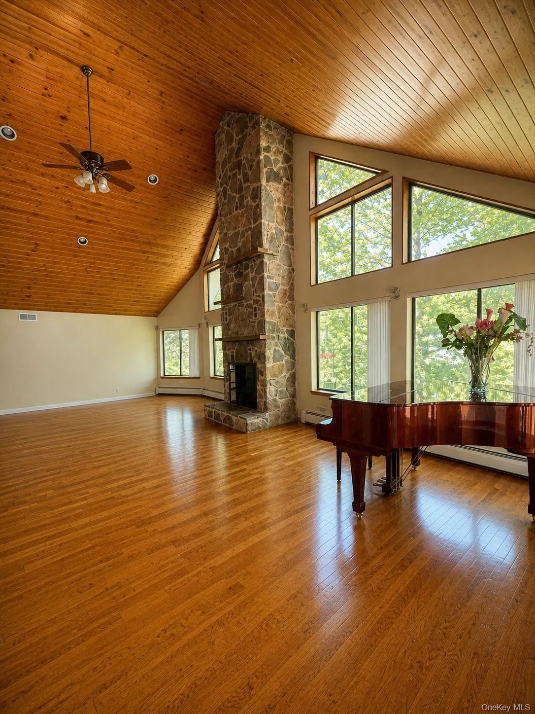 Spacious room featuring wood-finish flooring, a vaulted wood-paneled ceiling, a stone fireplace, large windows, and recessed lighting Spacious room featuring wood-finish flooring, a vaulted wood-paneled ceiling, a stone fireplace, large windows, and recessed lighting