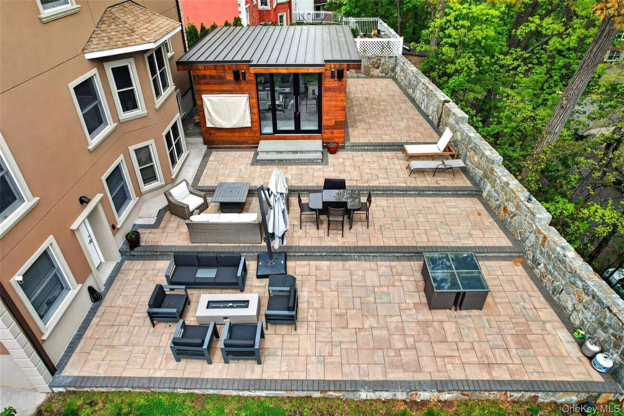 Multi-level paver patio featuring stone retaining walls and a detached structure with wood siding and a metal roof Multi-level paver patio featuring stone retaining walls and a detached structure with wood siding and a metal roof