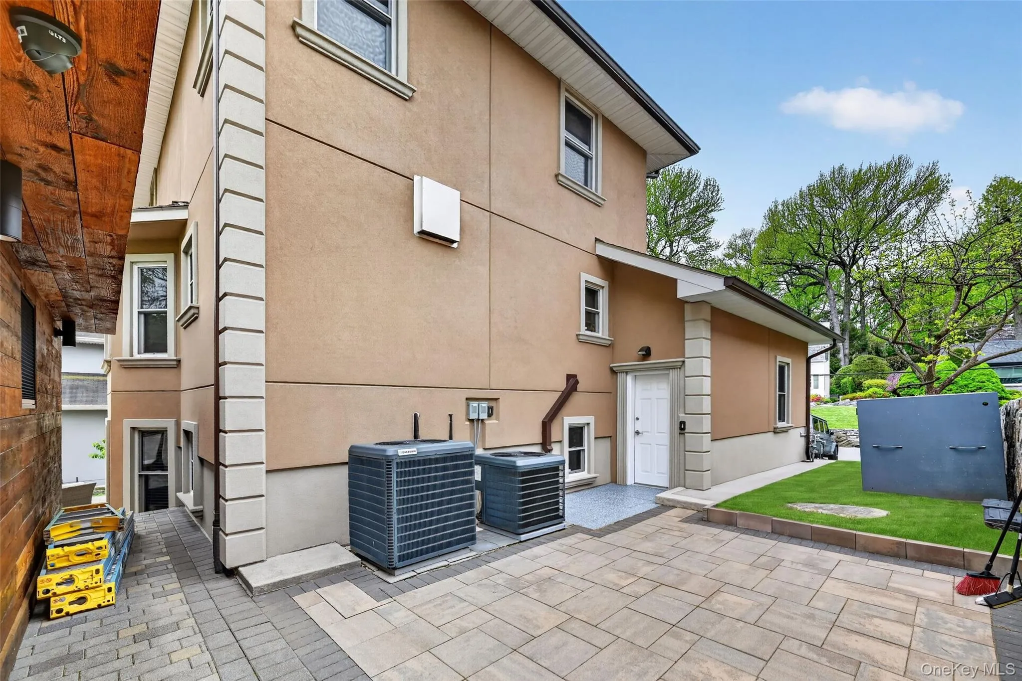 Exterior featuring stucco finish, decorative trim, multiple windows, a white entry door, and a paved patio area Exterior featuring stucco finish, decorative trim, multiple windows, a white entry door, and a paved patio area