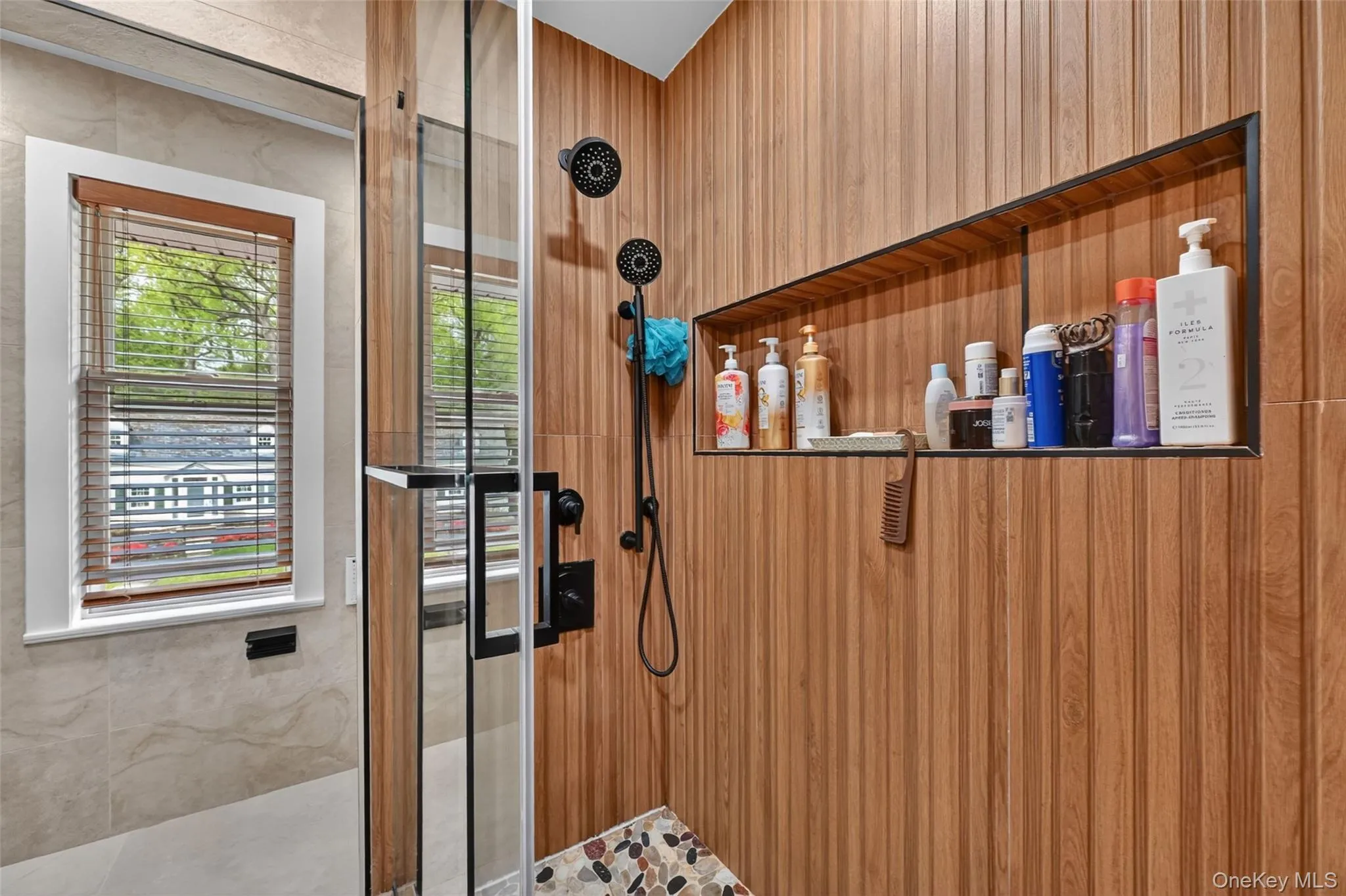 Shower enclosure featuring glass doors, wood-finish wall panels, a built-in recessed shelf with a dark frame, and matte black shower fixtures Shower enclosure featuring glass doors, wood-finish wall panels, a built-in recessed shelf with a dark frame, and matte black shower fixtures