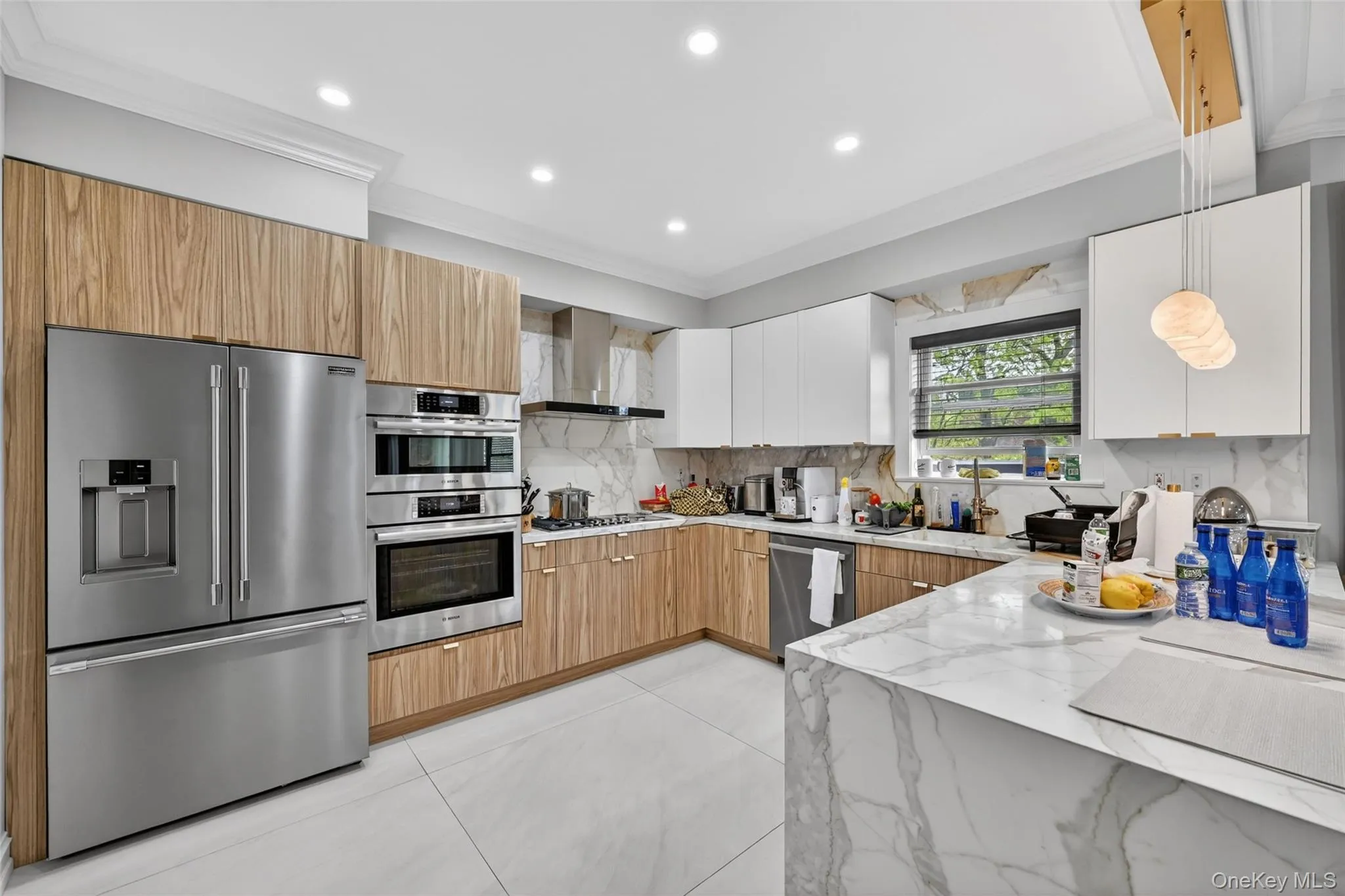 Contemporary kitchen featuring wood-finish and white cabinetry, stainless steel appliances including a built-in oven and microwave, a gas range with a range hood, and a waterfall-edge island with a marble-style surface Contemporary kitchen featuring wood-finish and white cabinetry, stainless steel appliances including a built-in oven and microwave, a gas range with a range hood, and a waterfall-edge island with a marble-style surface