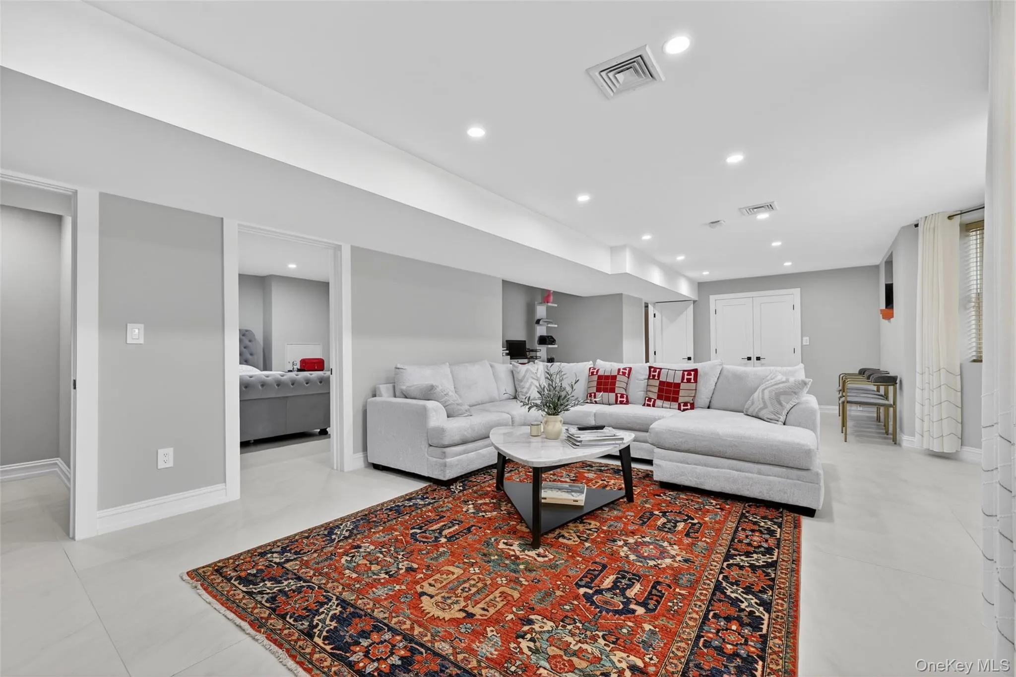Spacious living area featuring light gray walls, recessed lighting, and large format light-toned tile flooring Spacious living area featuring light gray walls, recessed lighting, and large format light-toned tile flooring