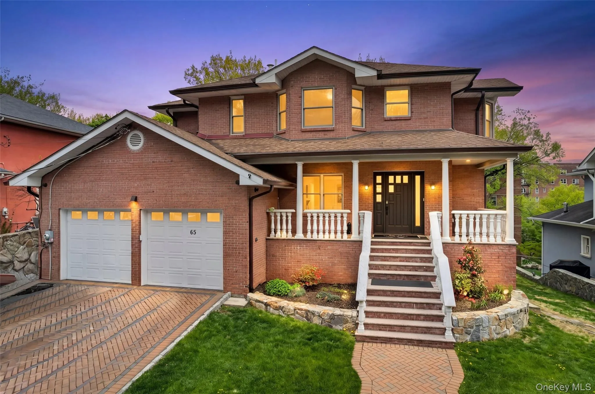 Brick residence featuring a two-car garage with individual doors, a paved driveway, and a front porch with white railings and columns Brick residence featuring a two-car garage with individual doors, a paved driveway, and a front porch with white railings and columns