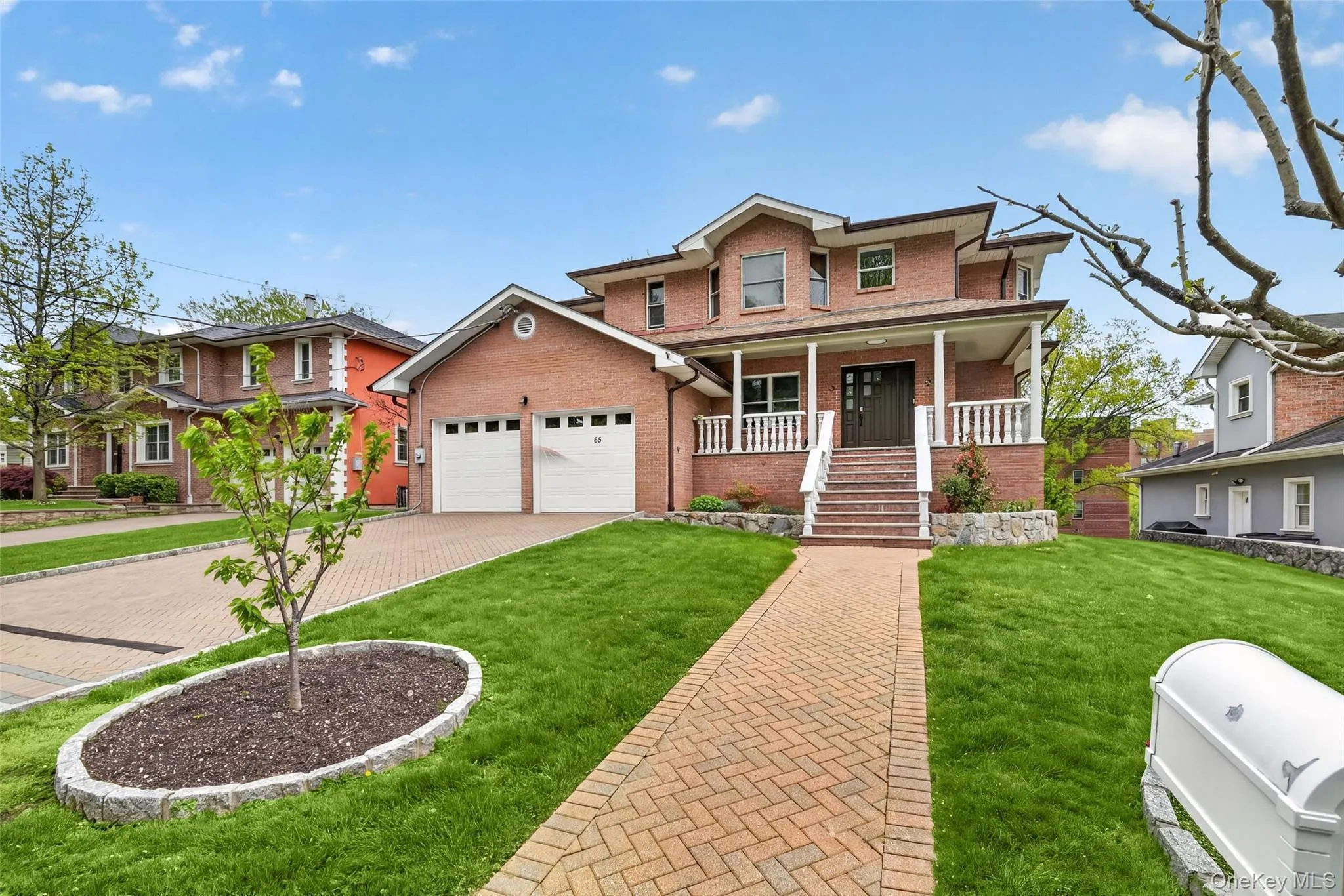 Brick facade residence with a two-car garage, covered front porch, and a patterned paver driveway Brick facade residence with a two-car garage, covered front porch, and a patterned paver driveway
