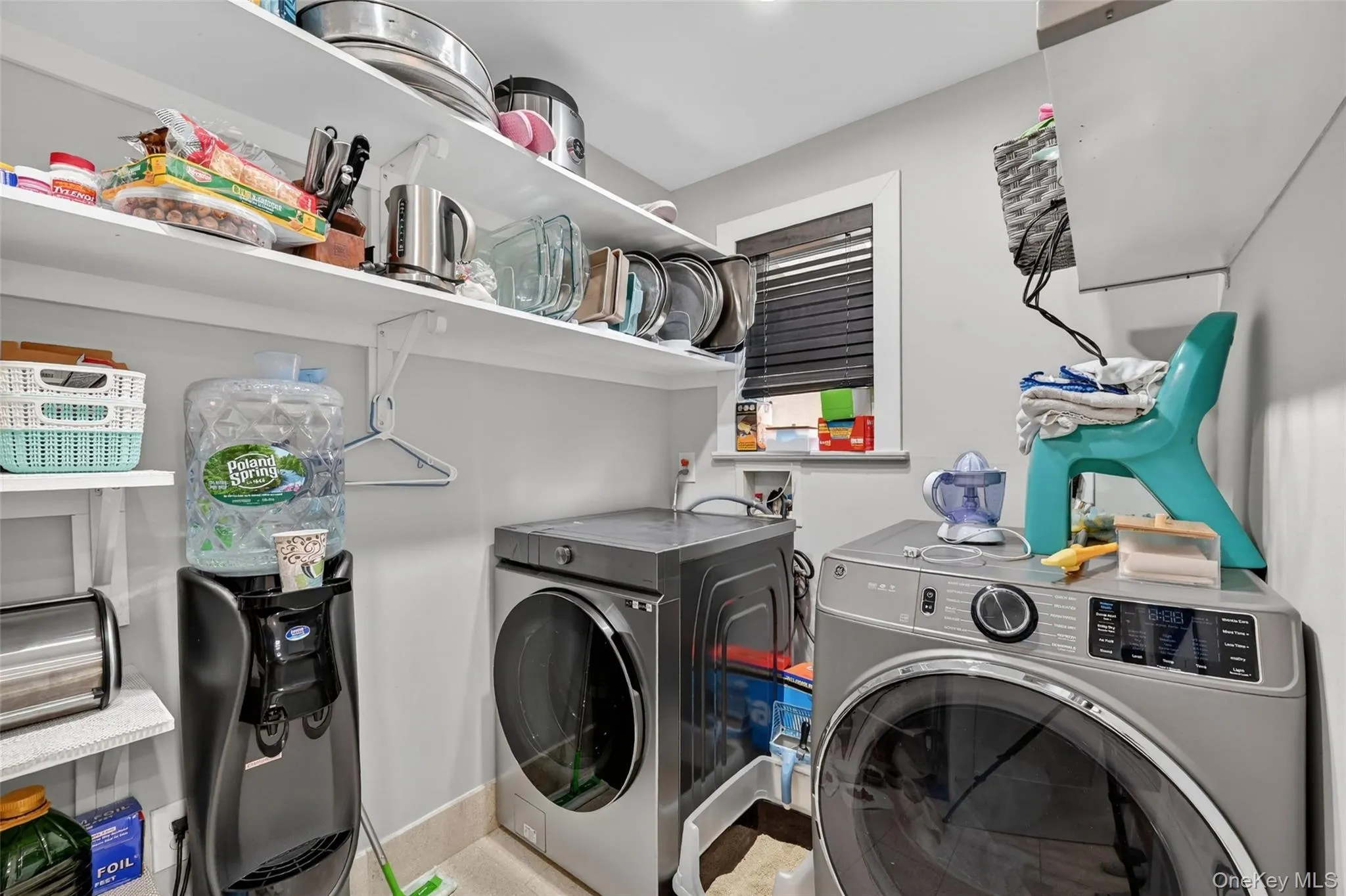 Dedicated utility space featuring a front-load washer and dryer, ample shelving for storage, and a single window with blinds Dedicated utility space featuring a front-load washer and dryer, ample shelving for storage, and a single window with blinds