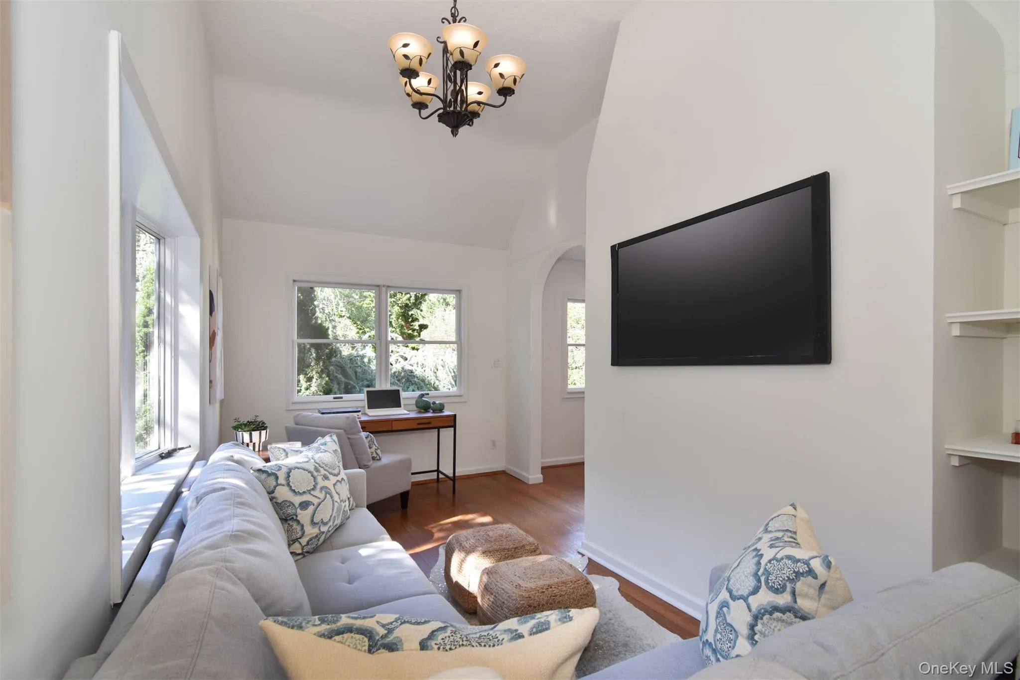 Living area with wood finished floors, arched walkways, a desk, high vaulted ceiling, and a chandelier Living area with wood finished floors, arched walkways, a desk, high vaulted ceiling, and a chandelier