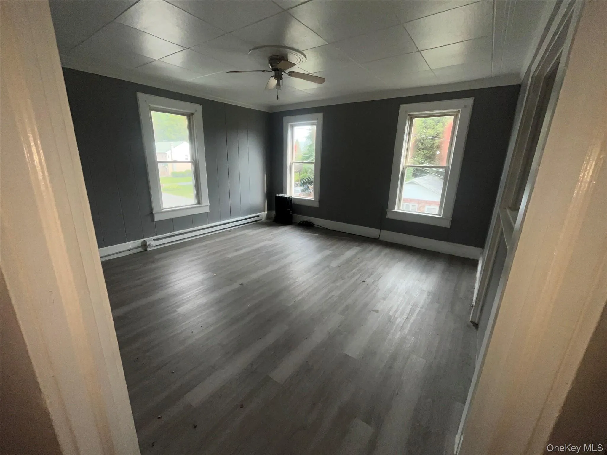 Empty room with dark wood-style floors, a baseboard heating unit, and ceiling fan Empty room with dark wood-style floors, a baseboard heating unit, and ceiling fan