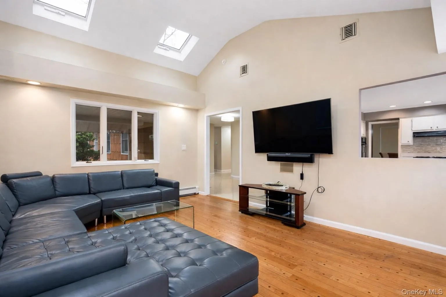 Living room with light wood-style flooring, vaulted ceiling, baseboard heating, recessed lighting, and a skylight Living room with light wood-style flooring, vaulted ceiling, baseboard heating, recessed lighting, and a skylight