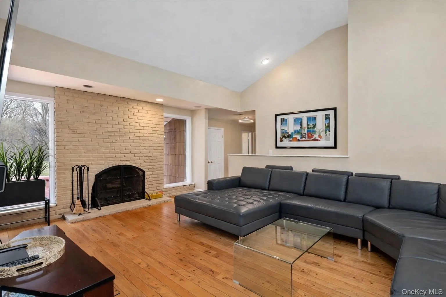Living room with lofted ceiling, light wood-style flooring, and a brick fireplace Living room with lofted ceiling, light wood-style flooring, and a brick fireplace