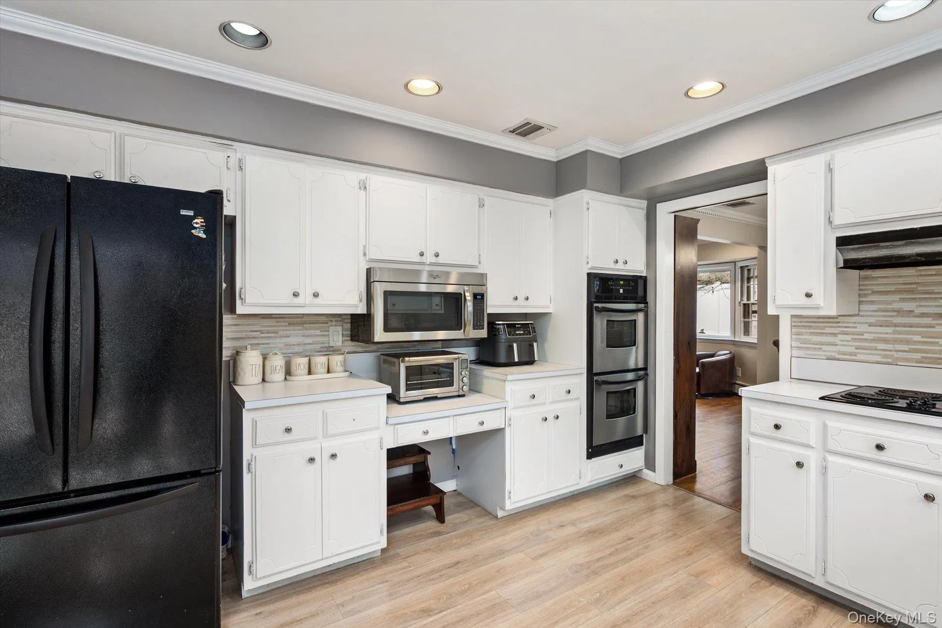 Kitchen featuring tasteful backsplash, black appliances, ornamental molding, light countertops, and light wood-style flooring Kitchen featuring tasteful backsplash, black appliances, ornamental molding, light countertops, and light wood-style flooring