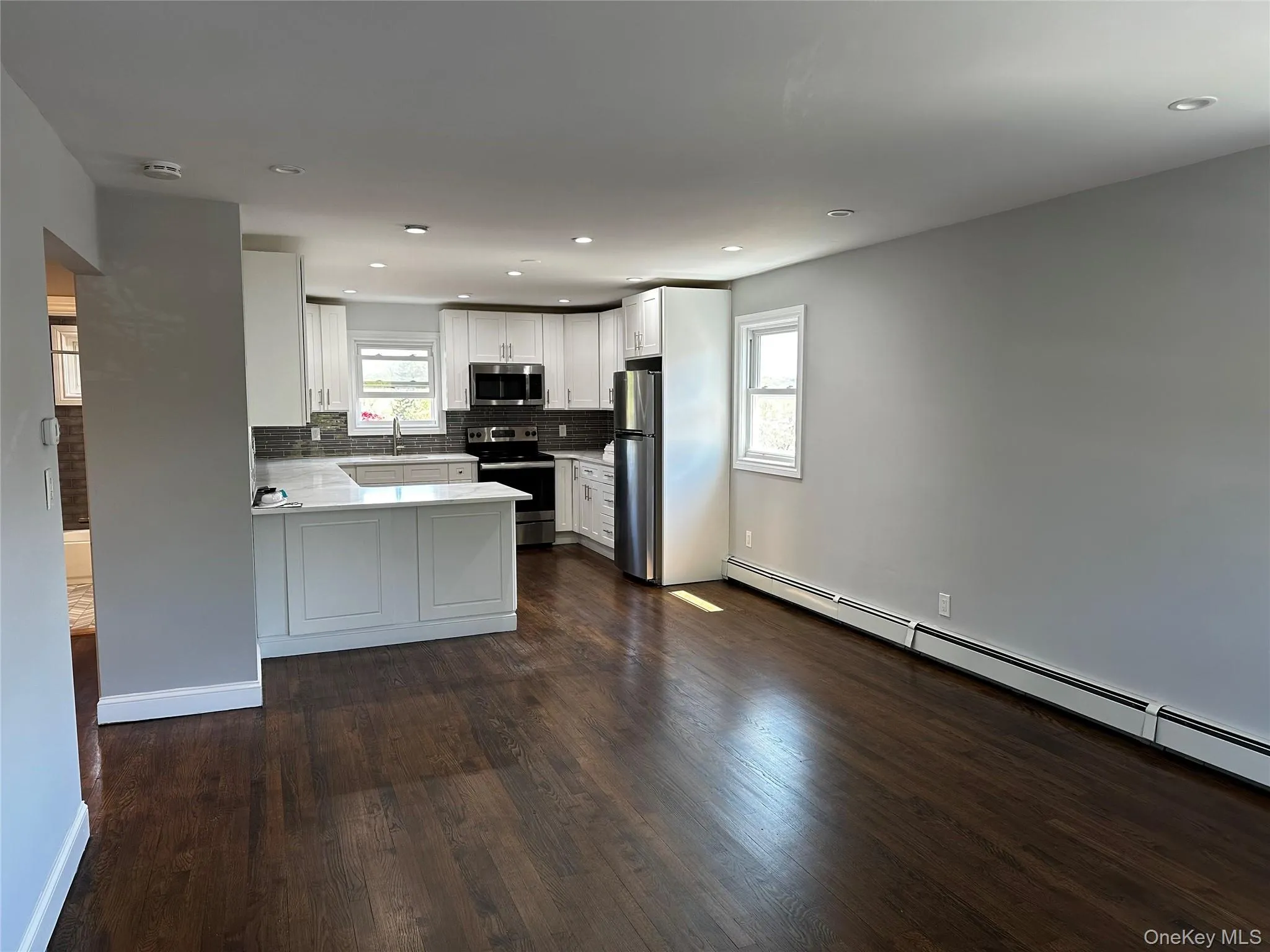 Open-concept living space featuring wood-finish flooring, recessed lighting, and a kitchen with white cabinetry, stainless steel appliances, and a peninsula countertop Open-concept living space featuring wood-finish flooring, recessed lighting, and a kitchen with white cabinetry, stainless steel appliances, and a peninsula countertop