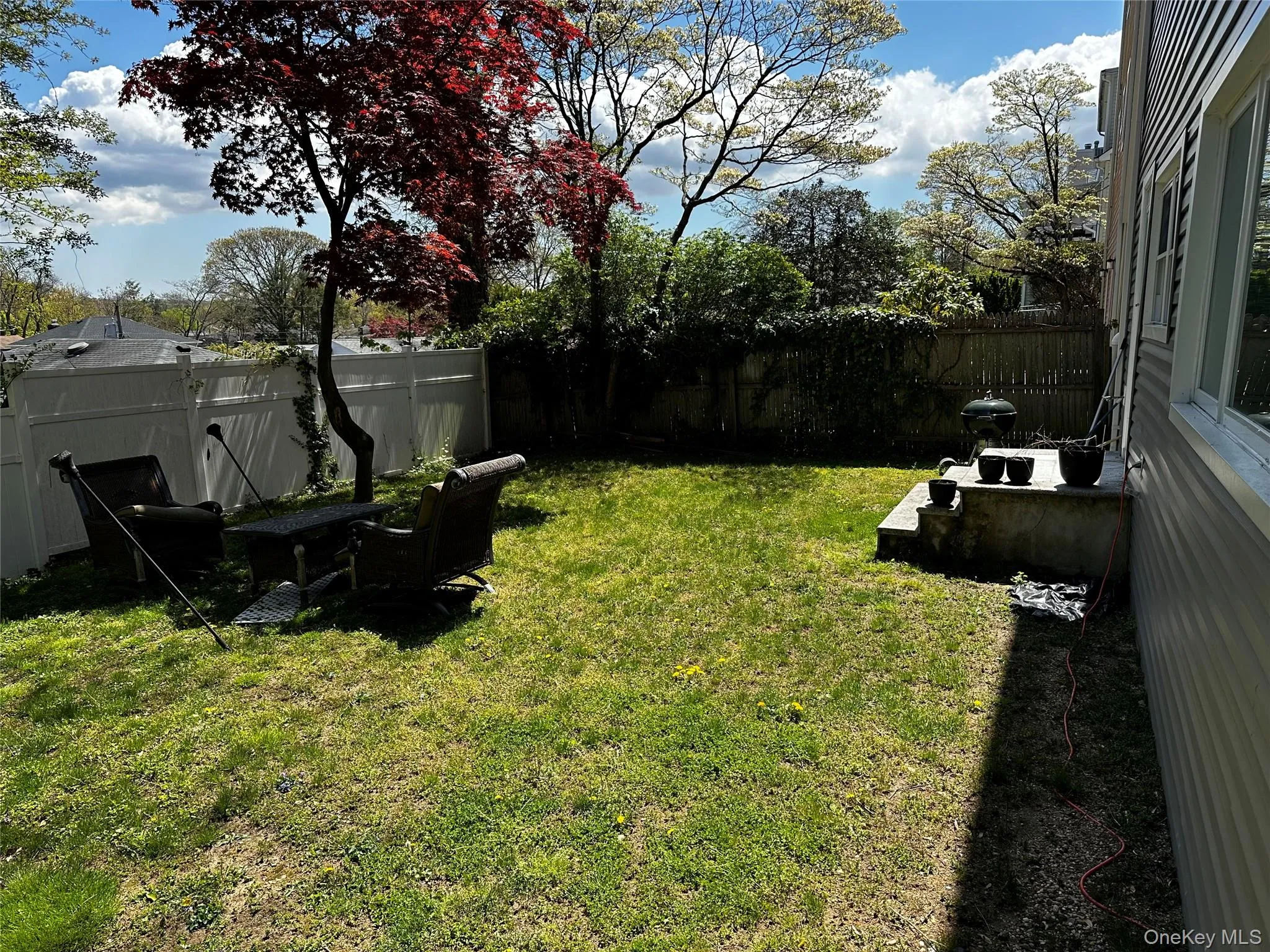 Expansive backyard featuring a lush lawn, mature trees, white vinyl fencing, a concrete patio, and exterior siding Expansive backyard featuring a lush lawn, mature trees, white vinyl fencing, a concrete patio, and exterior siding