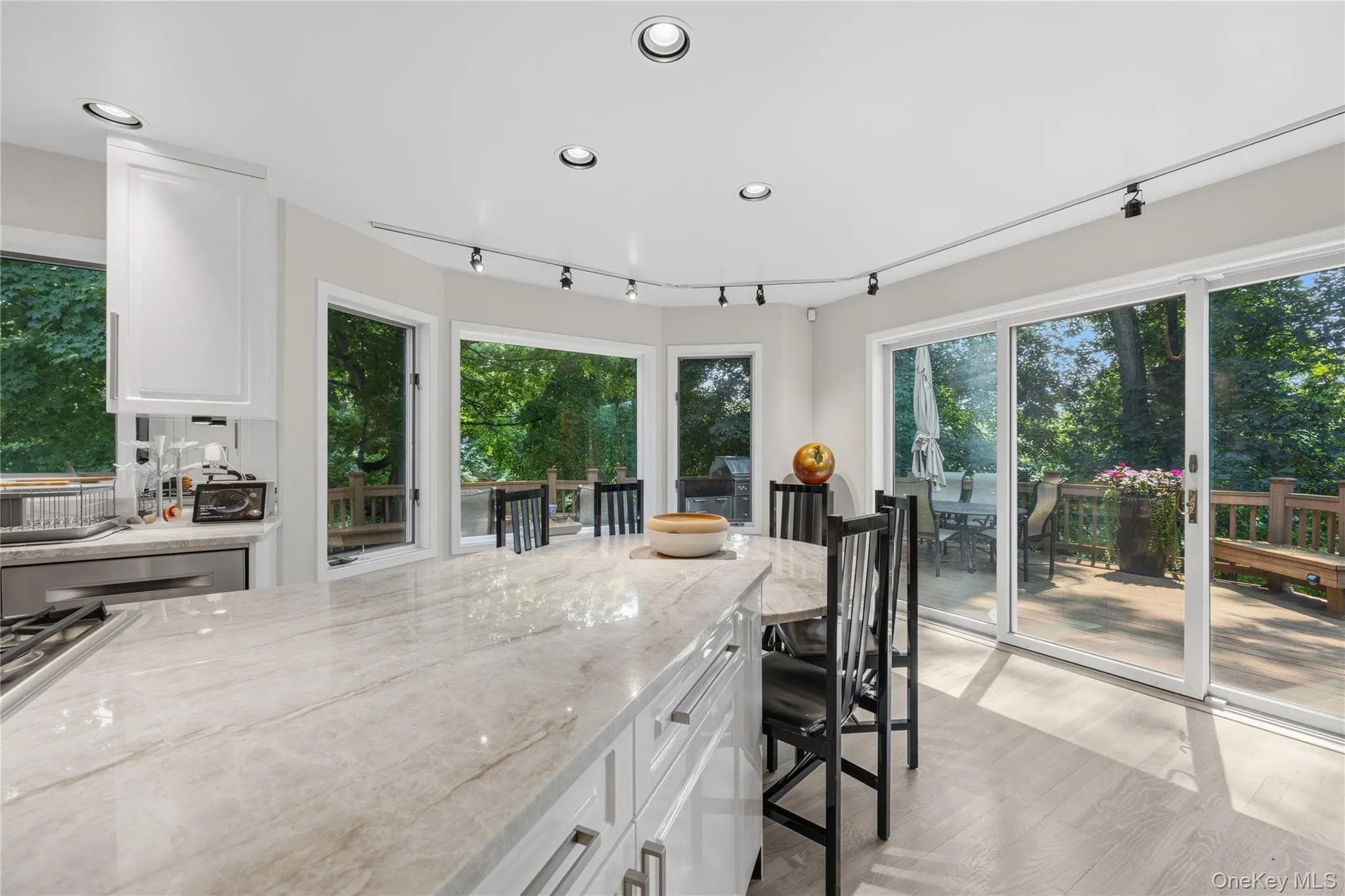View from inside the gleeaming white kitchen with walls of windows and sliding glass doors to the wrap-around deck with another outside kitchen area. View from inside the gleeaming white kitchen with walls of windows and sliding glass doors to the wrap-around deck with another outside kitchen area.
