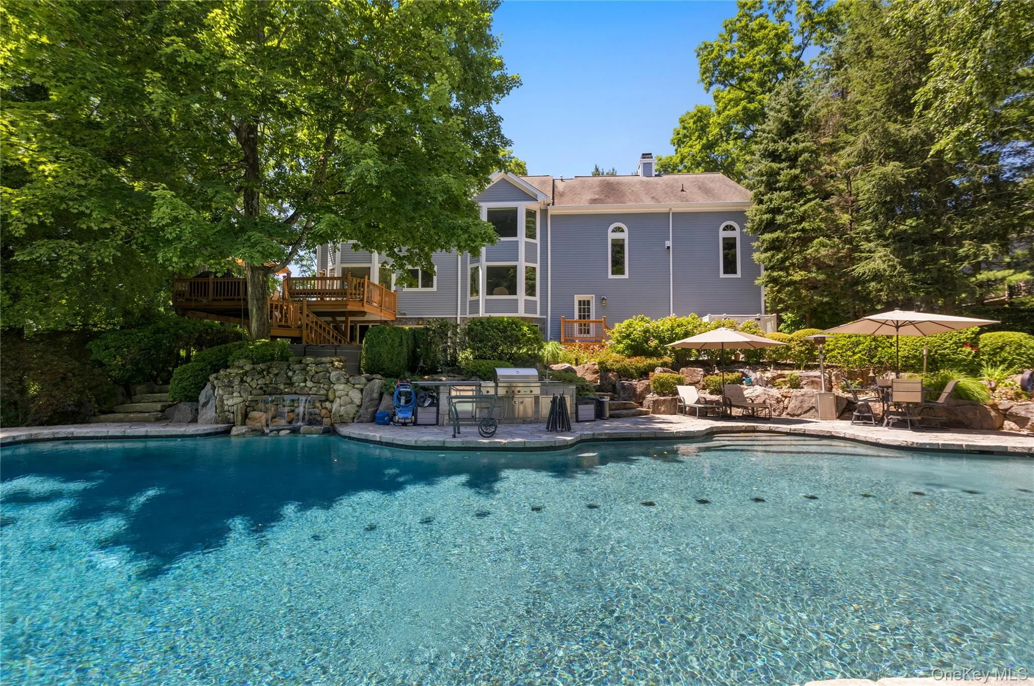 Rear view of house, deck, pool, patio and outdoor kitchen on a summer day. Rear view of house, deck, pool, patio and outdoor kitchen on a summer day.