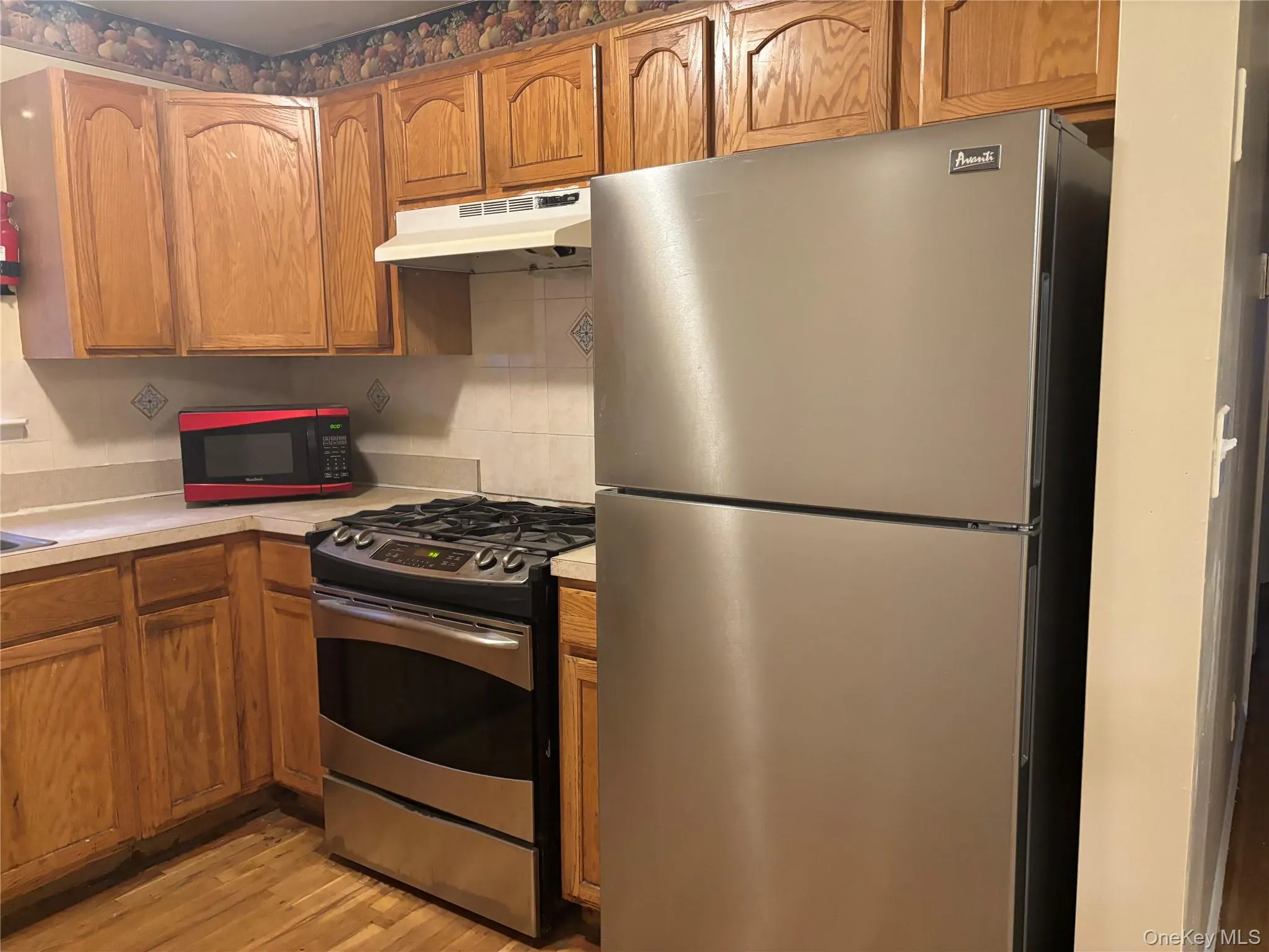 Kitchen featuring wood cabinetry, light-toned countertops, a stainless steel refrigerator, and a stainless steel range with overhead ventilation Kitchen featuring wood cabinetry, light-toned countertops, a stainless steel refrigerator, and a stainless steel range with overhead ventilation
