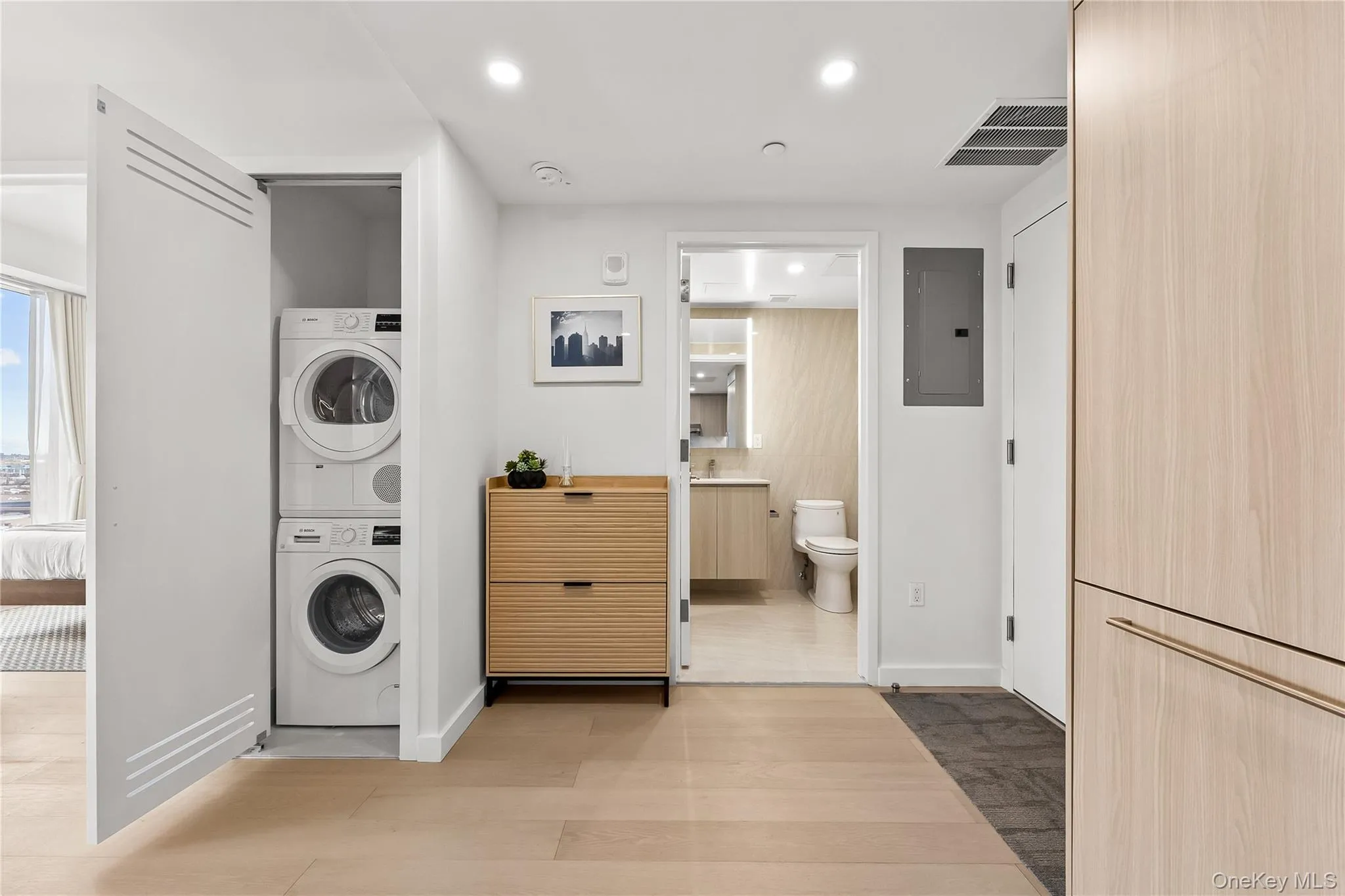 Laundry room with stacked washing machine and dryer, electric panel, light wood-type flooring, and recessed lighting Laundry room with stacked washing machine and dryer, electric panel, light wood-type flooring, and recessed lighting