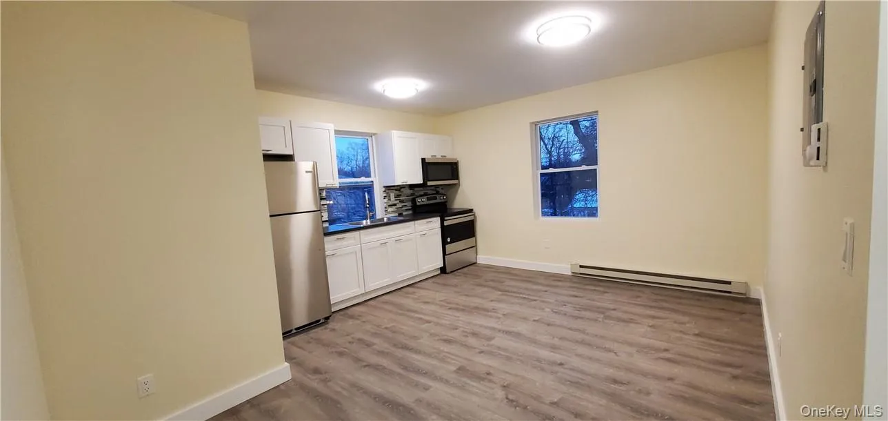 Kitchen area featuring stainless steel appliances, white cabinetry, dark countertops, and a mosaic tile backsplash Kitchen area featuring stainless steel appliances, white cabinetry, dark countertops, and a mosaic tile backsplash