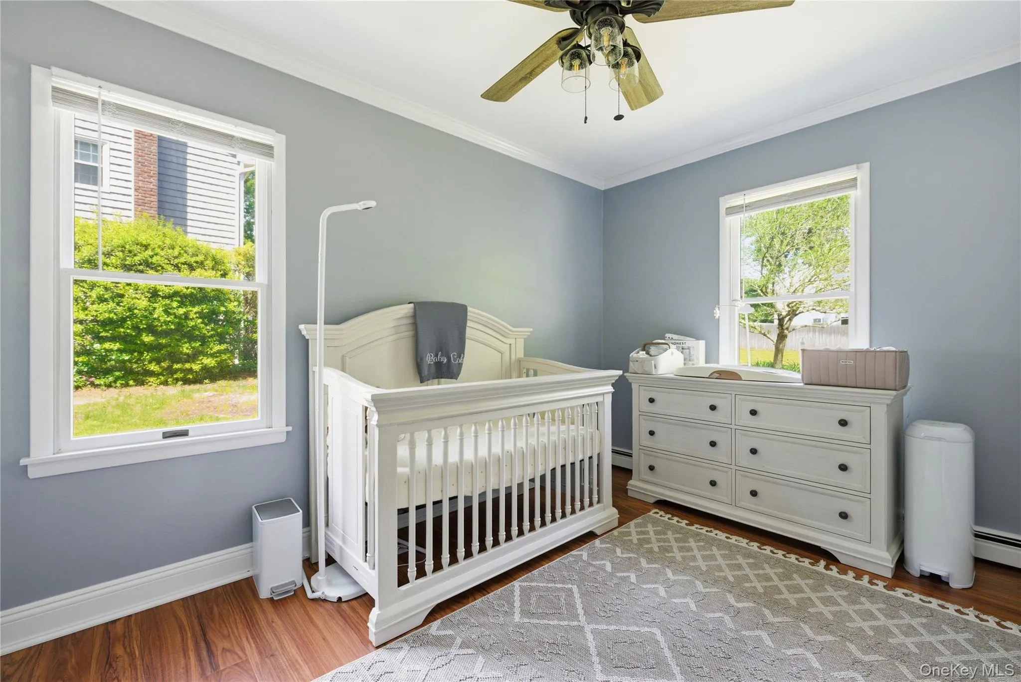 Spacious room featuring wood-finish flooring, two large windows, a ceiling fan, and crown molding Spacious room featuring wood-finish flooring, two large windows, a ceiling fan, and crown molding