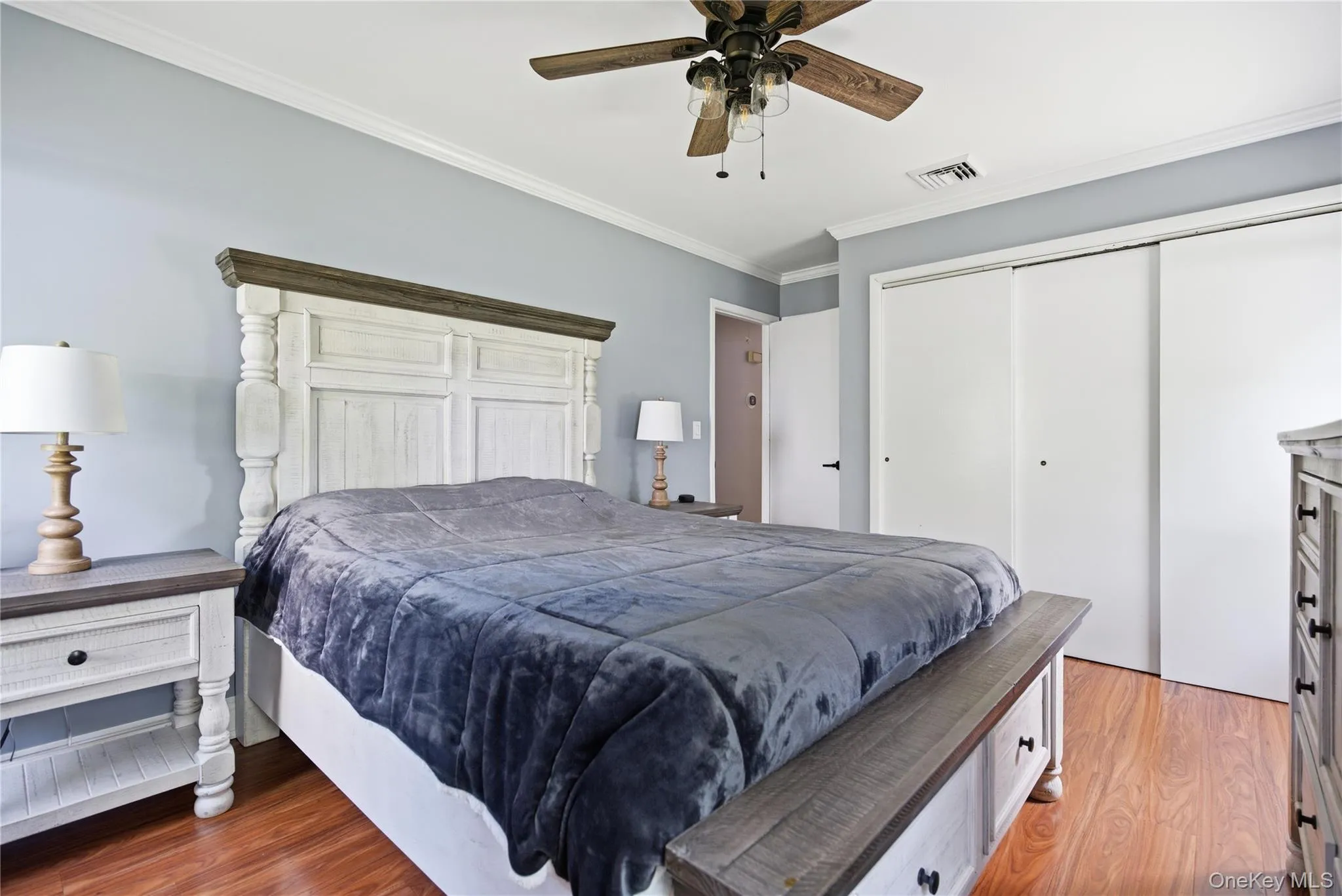Room featuring wood-finish flooring, light blue walls, white crown molding, and a ceiling fan with light fixture Room featuring wood-finish flooring, light blue walls, white crown molding, and a ceiling fan with light fixture