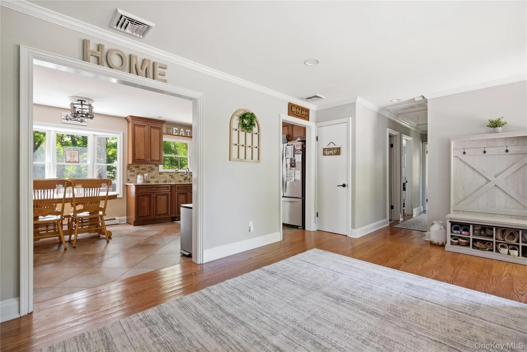 Hardwood flooring extends throughout this interior space, featuring a wide doorway opening to a kitchen with warm wood cabinetry and a tile backsplash Hardwood flooring extends throughout this interior space, featuring a wide doorway opening to a kitchen with warm wood cabinetry and a tile backsplash