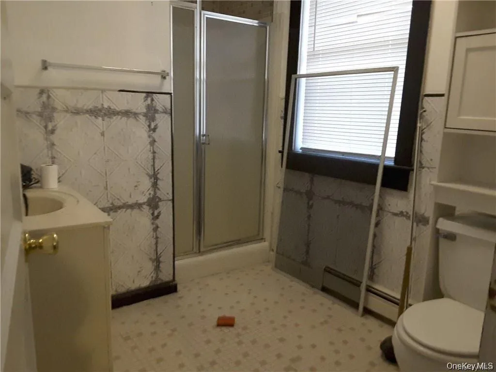 Bathroom featuring a glass-enclosed shower, a vanity with a drop-in sink, a toilet, a window with blinds, and tiled flooring Bathroom featuring a glass-enclosed shower, a vanity with a drop-in sink, a toilet, a window with blinds, and tiled flooring