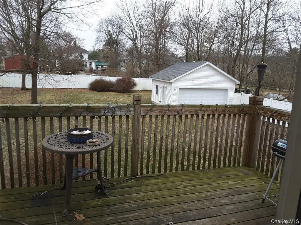 Spacious exterior deck with wood flooring and vertical wood railings, overlooking a detached garage with a white overhead door and a surrounding white fence Spacious exterior deck with wood flooring and vertical wood railings, overlooking a detached garage with a white overhead door and a surrounding white fence
