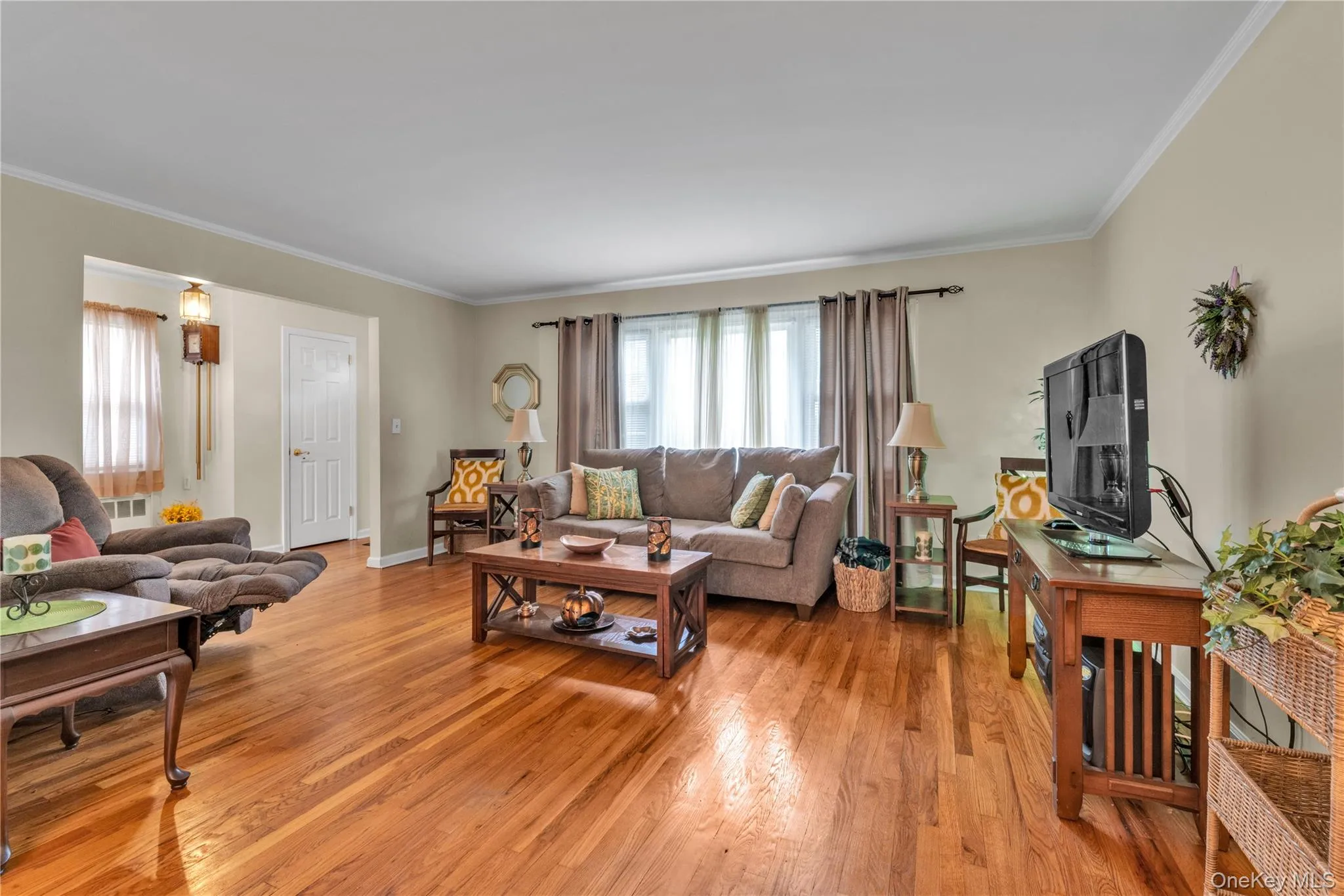 Bright living area featuring wood-finish flooring, neutral wall tones, and white crown molding Bright living area featuring wood-finish flooring, neutral wall tones, and white crown molding