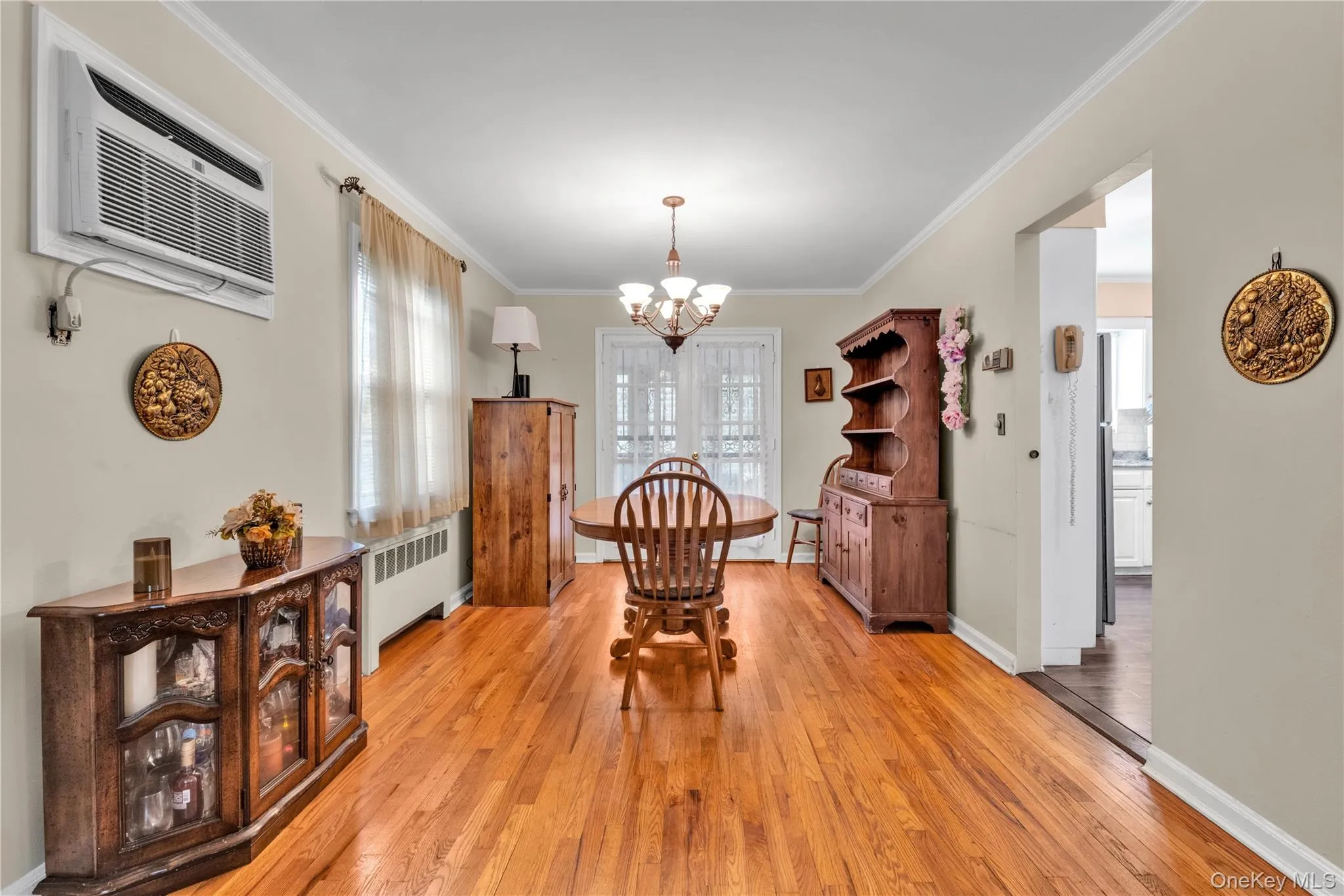 Spacious room featuring wood-finish flooring, a contemporary chandelier, crown molding, and an arched entry, and double doors to backyard. Spacious room featuring wood-finish flooring, a contemporary chandelier, crown molding, and an arched entry, and double doors to backyard.