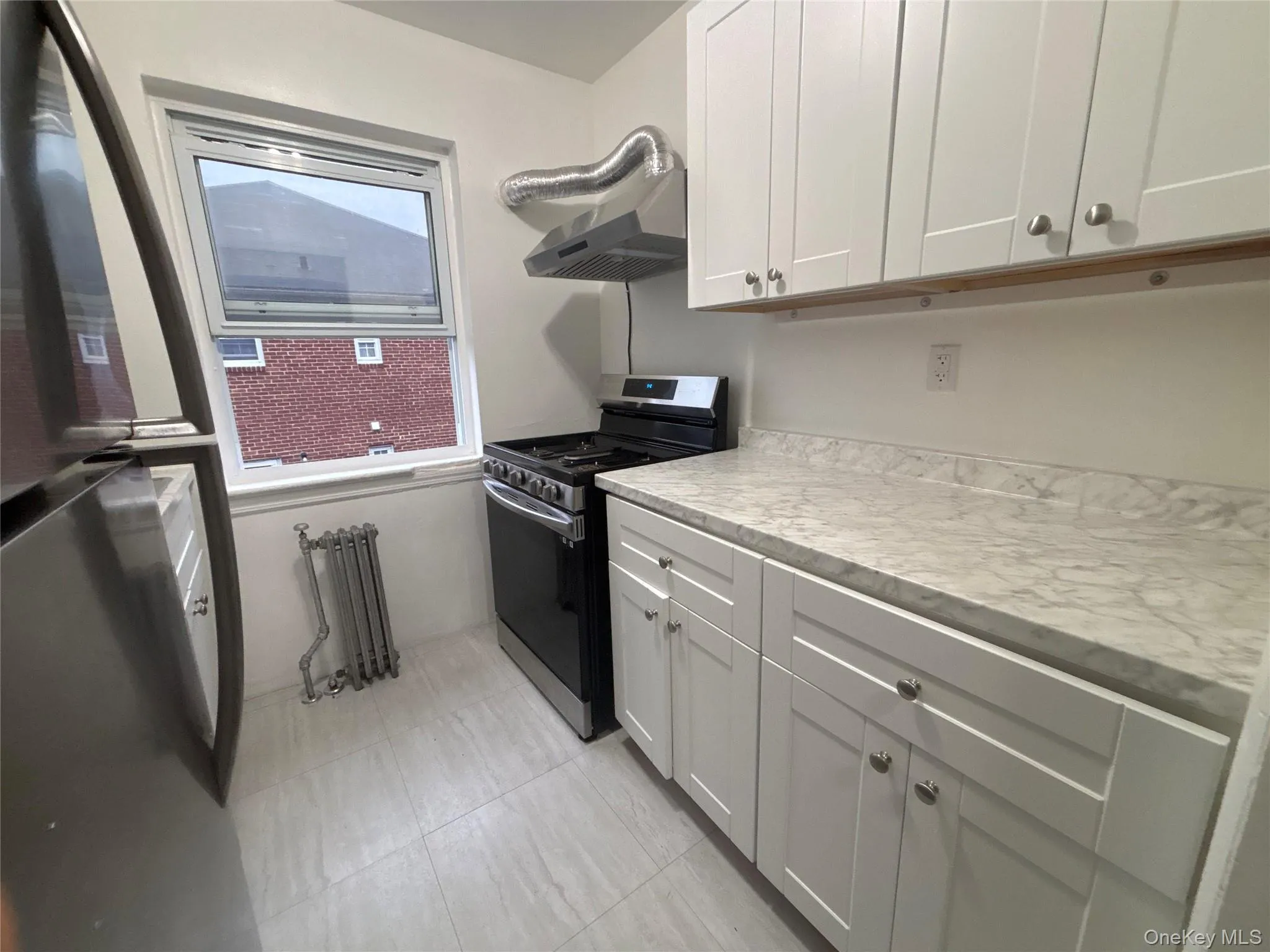 Kitchen with appliances with stainless steel finishes, light countertops, white cabinets, radiator, and extractor fan Kitchen with appliances with stainless steel finishes, light countertops, white cabinets, radiator, and extractor fan