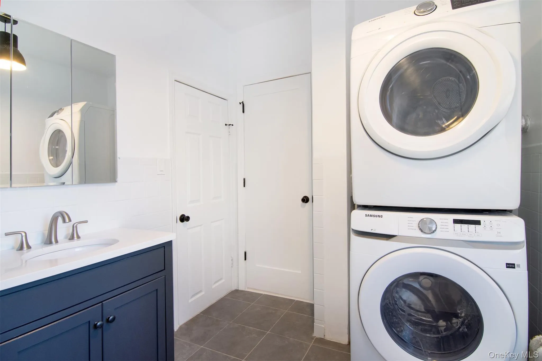 Bath room with dark tile patterned flooring, sink, stacked washer / dryer, and tile walls Bath room with dark tile patterned flooring, sink, stacked washer / dryer, and tile walls