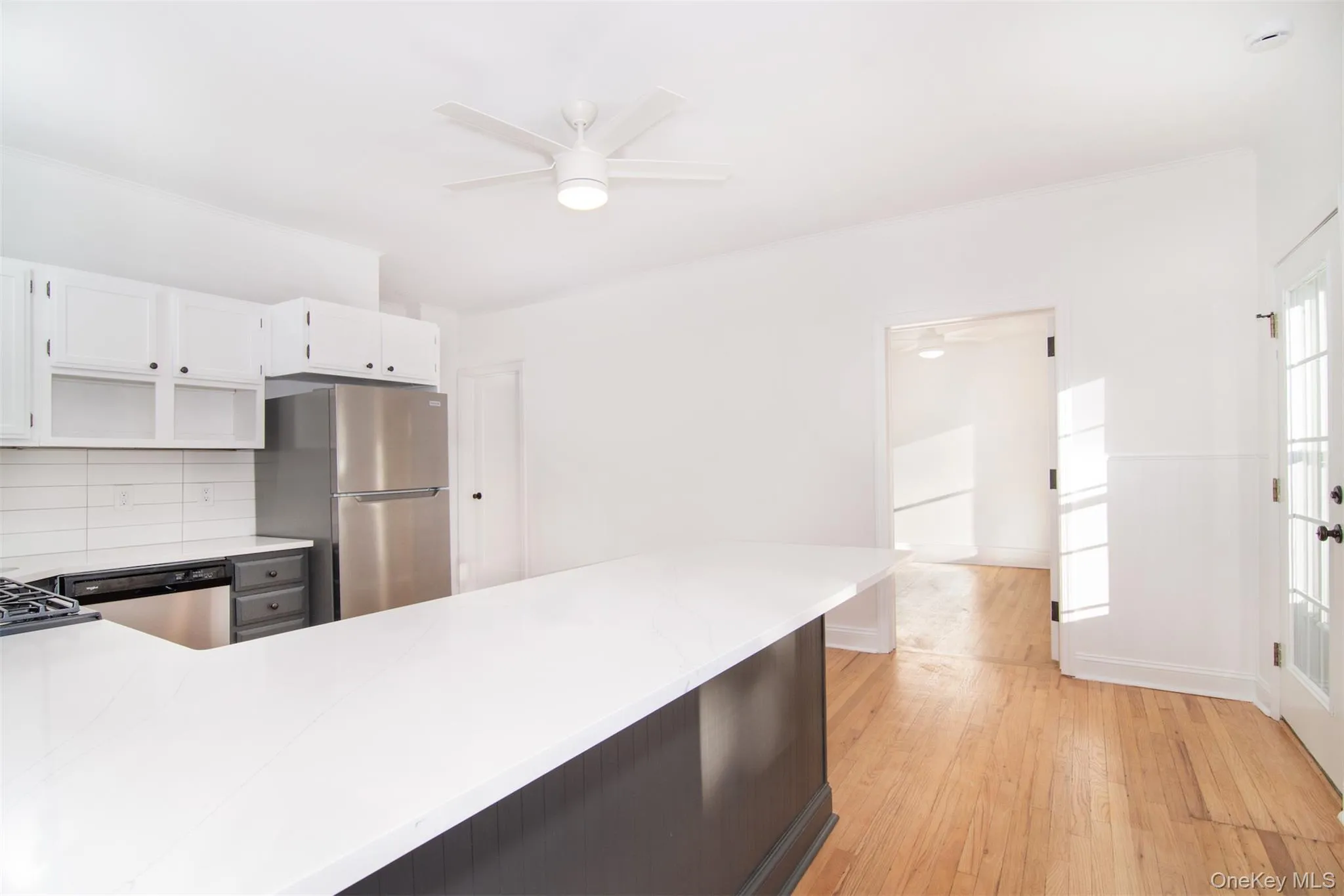 Kitchen with backsplash, white cabinets, light hardwood flooring, ceiling fan, and stainless steel appliances Kitchen with backsplash, white cabinets, light hardwood flooring, ceiling fan, and stainless steel appliances