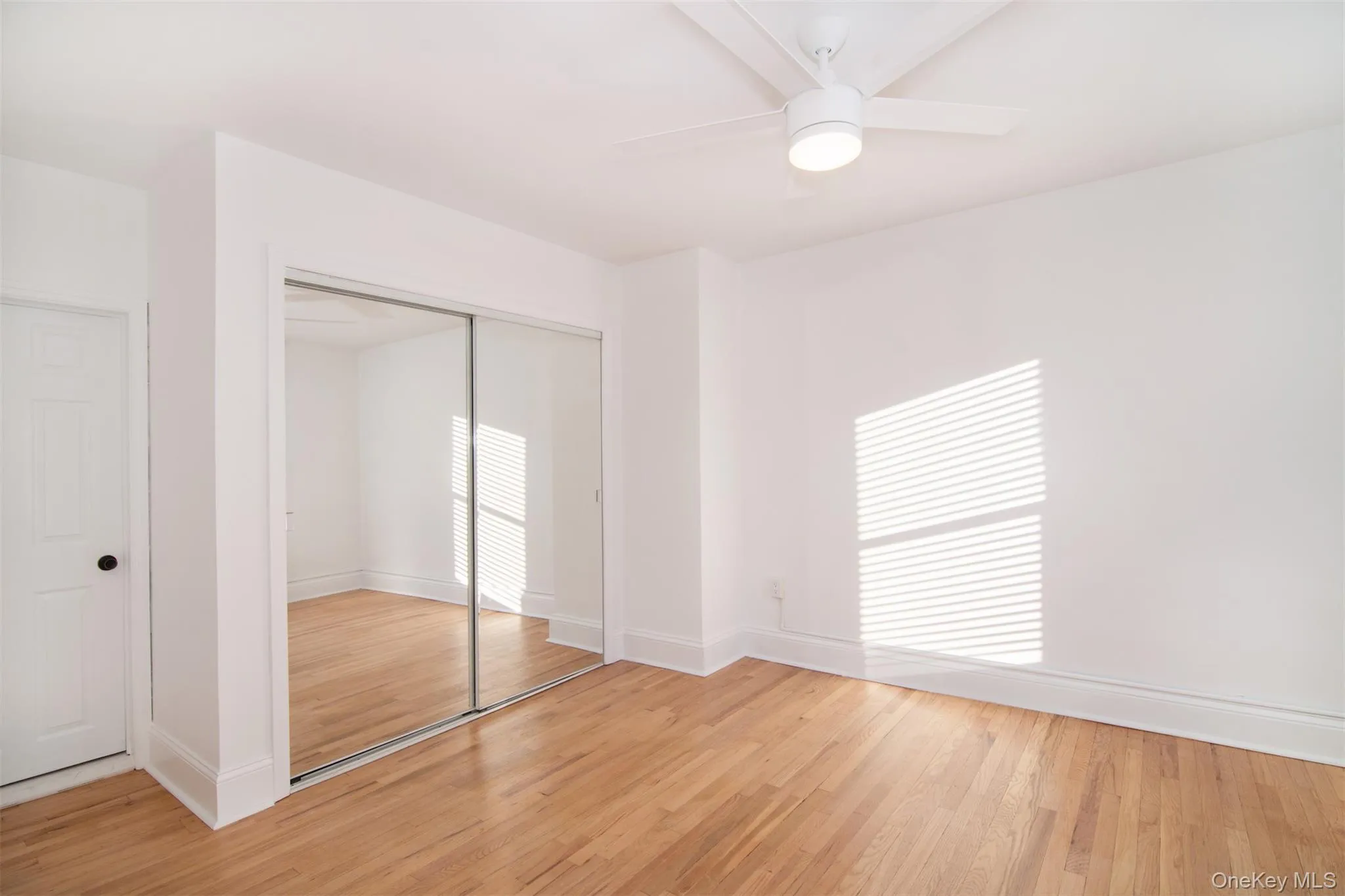 Unfurnished bedroom with a closet, ceiling fan, light hardwood flooring, and multiple windows Unfurnished bedroom with a closet, ceiling fan, light hardwood flooring, and multiple windows