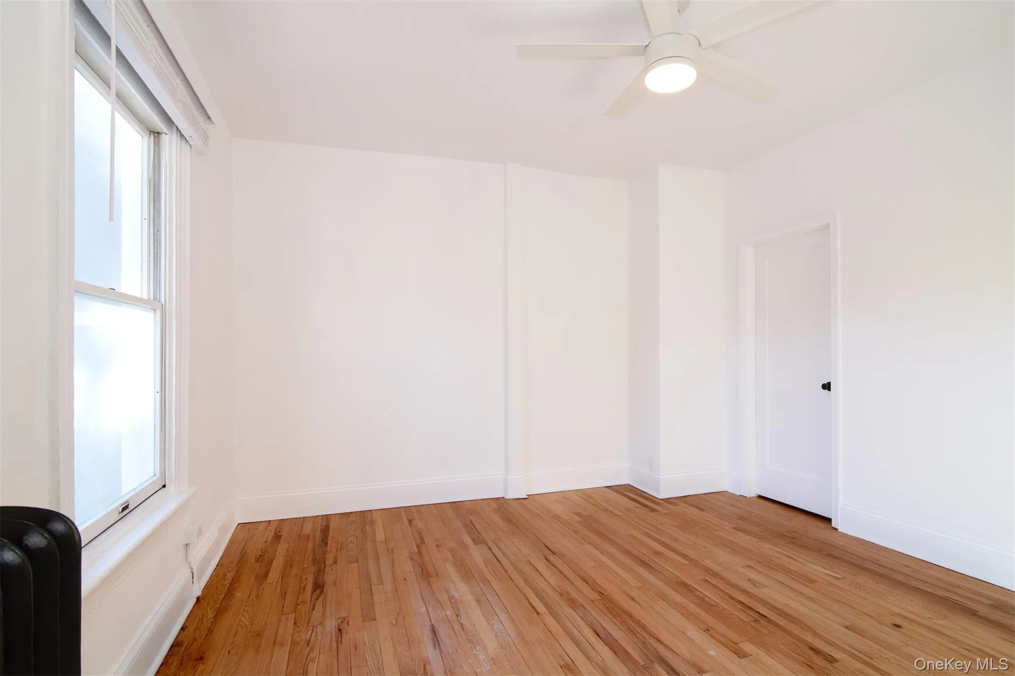 Living room with ceiling fan, radiator heating unit, and hardwood flooring Living room with ceiling fan, radiator heating unit, and hardwood flooring