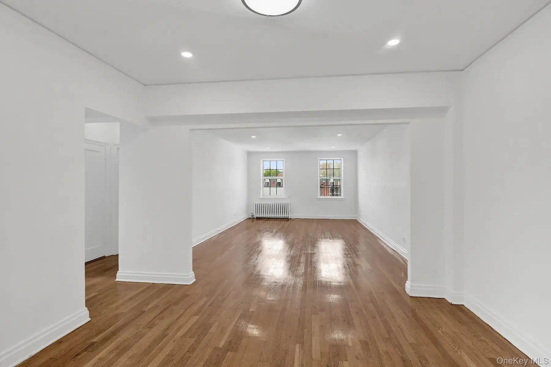 Spacious interior featuring wood-finish flooring, white painted walls, recessed lighting, and a white baseboard trim Spacious interior featuring wood-finish flooring, white painted walls, recessed lighting, and a white baseboard trim