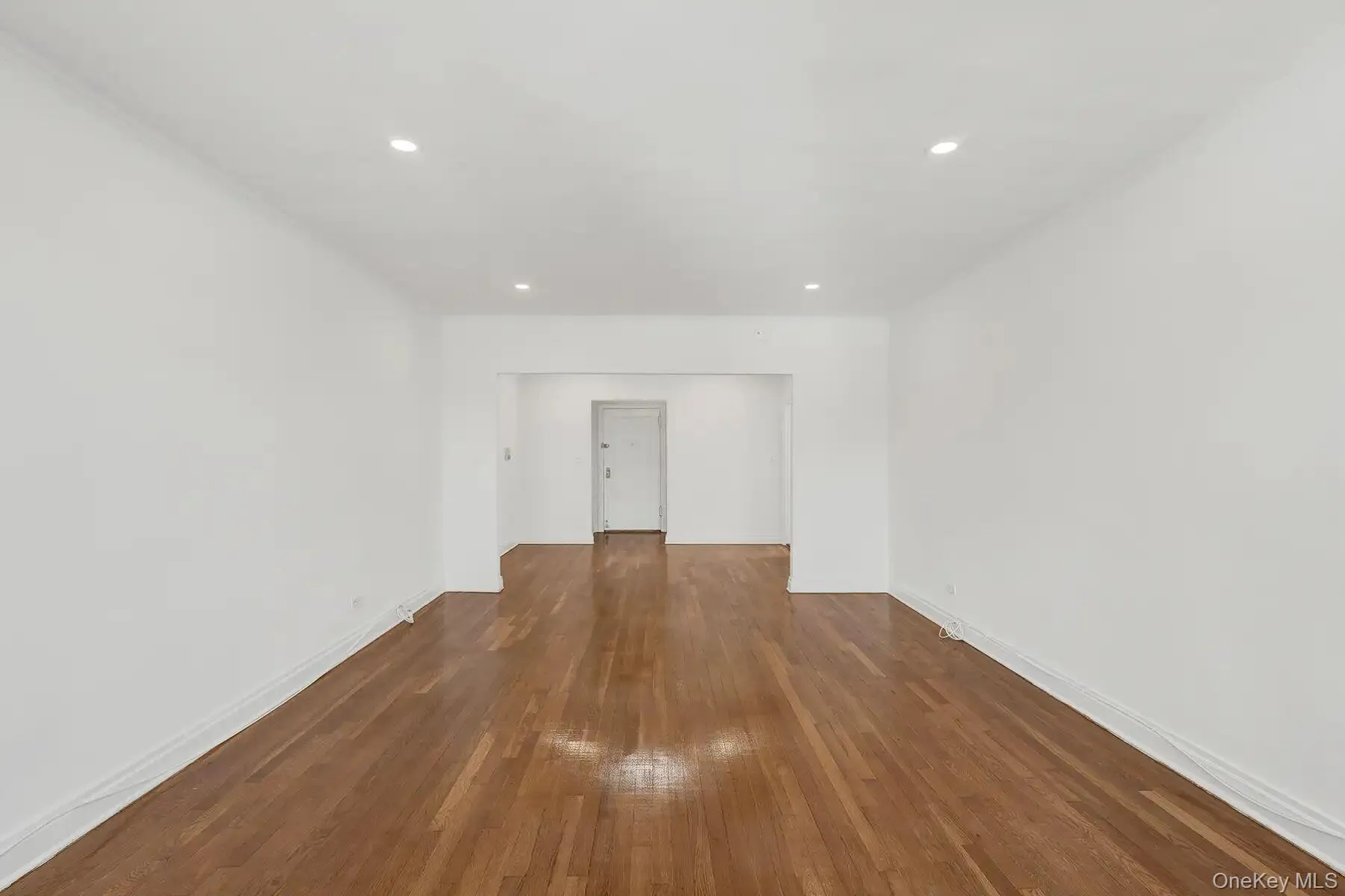 Expansive interior space featuring wood-finish flooring, white walls, recessed ceiling lighting, white baseboards, and a white ceiling Expansive interior space featuring wood-finish flooring, white walls, recessed ceiling lighting, white baseboards, and a white ceiling