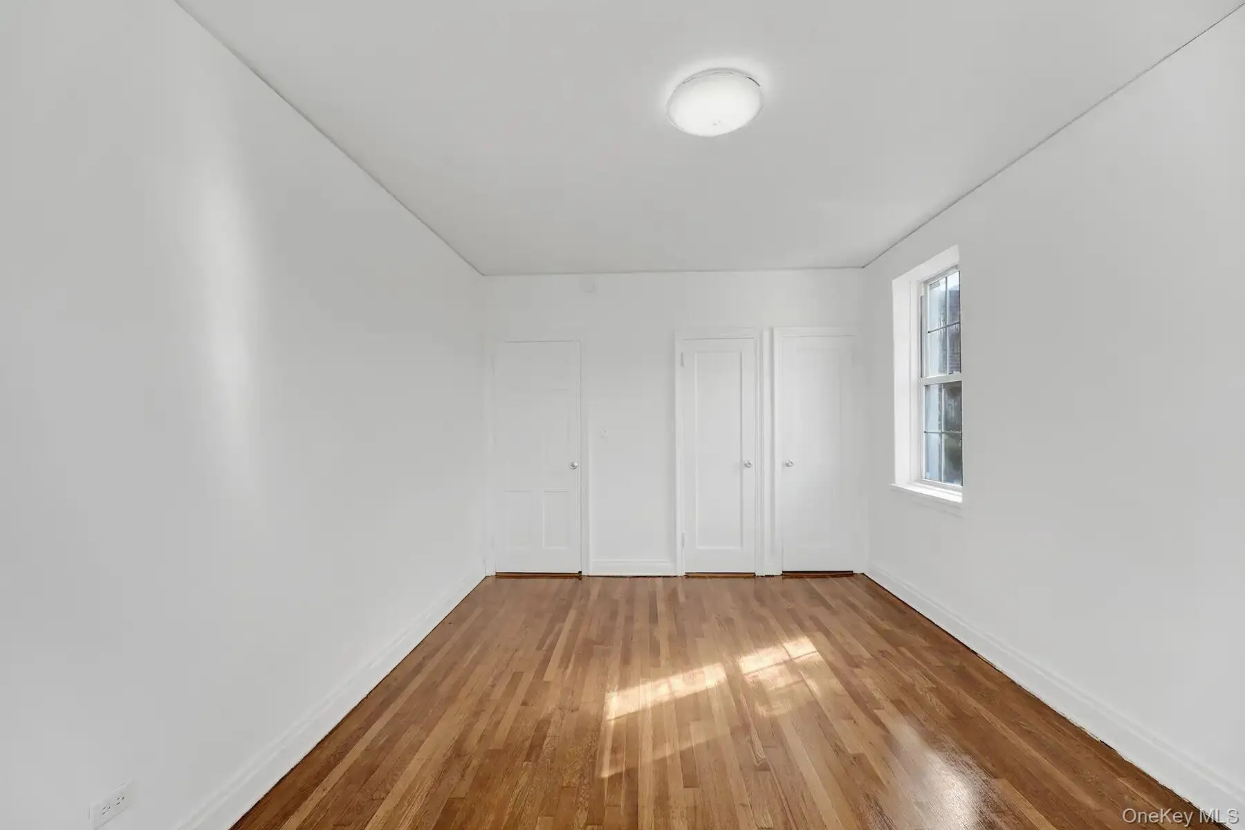 Bright room featuring wood-finish flooring, white walls, two panel doors, and a double-hung window Bright room featuring wood-finish flooring, white walls, two panel doors, and a double-hung window