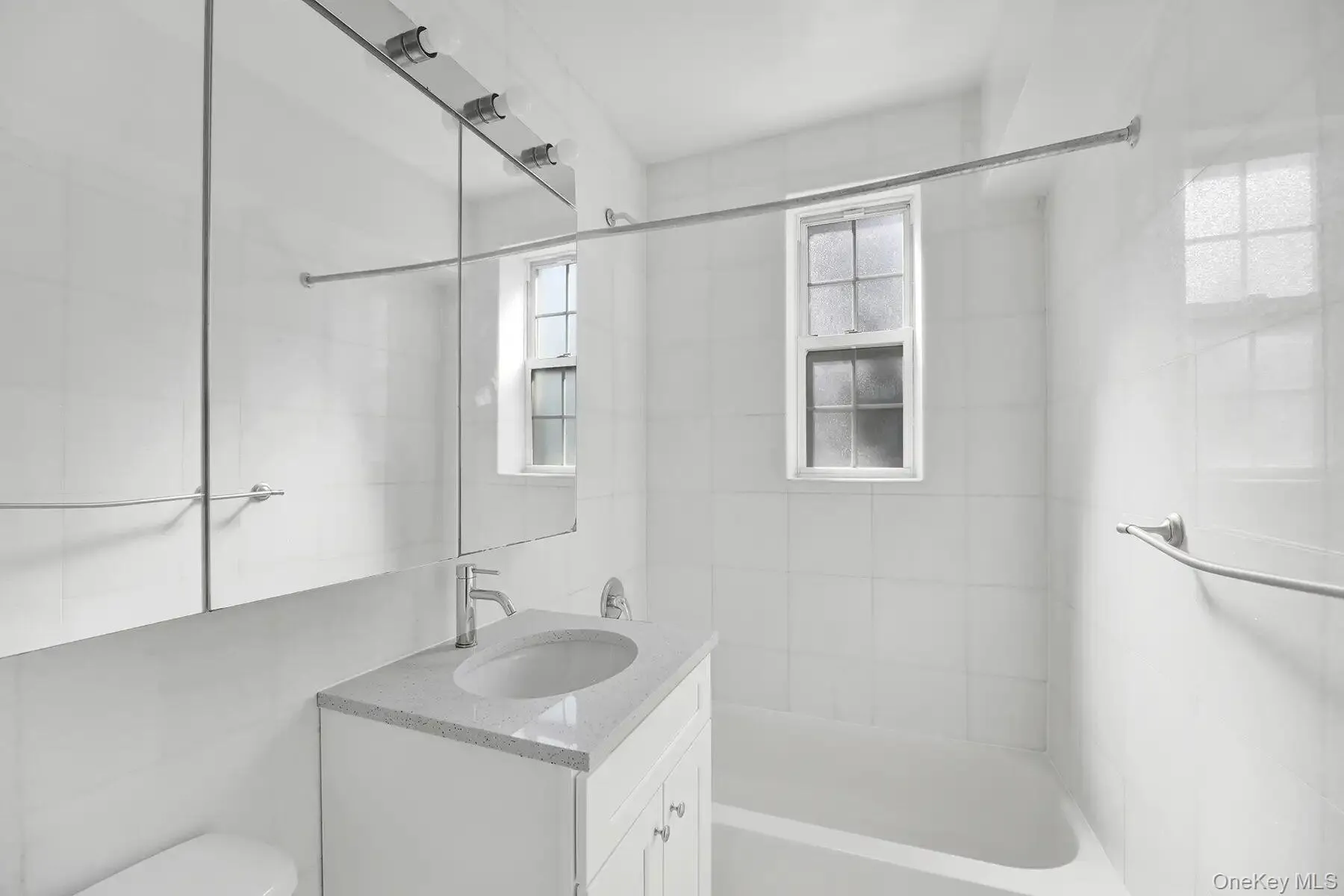 Bathroom featuring a white vanity with a light-toned countertop, an integrated sink, and chrome fixtures Bathroom featuring a white vanity with a light-toned countertop, an integrated sink, and chrome fixtures