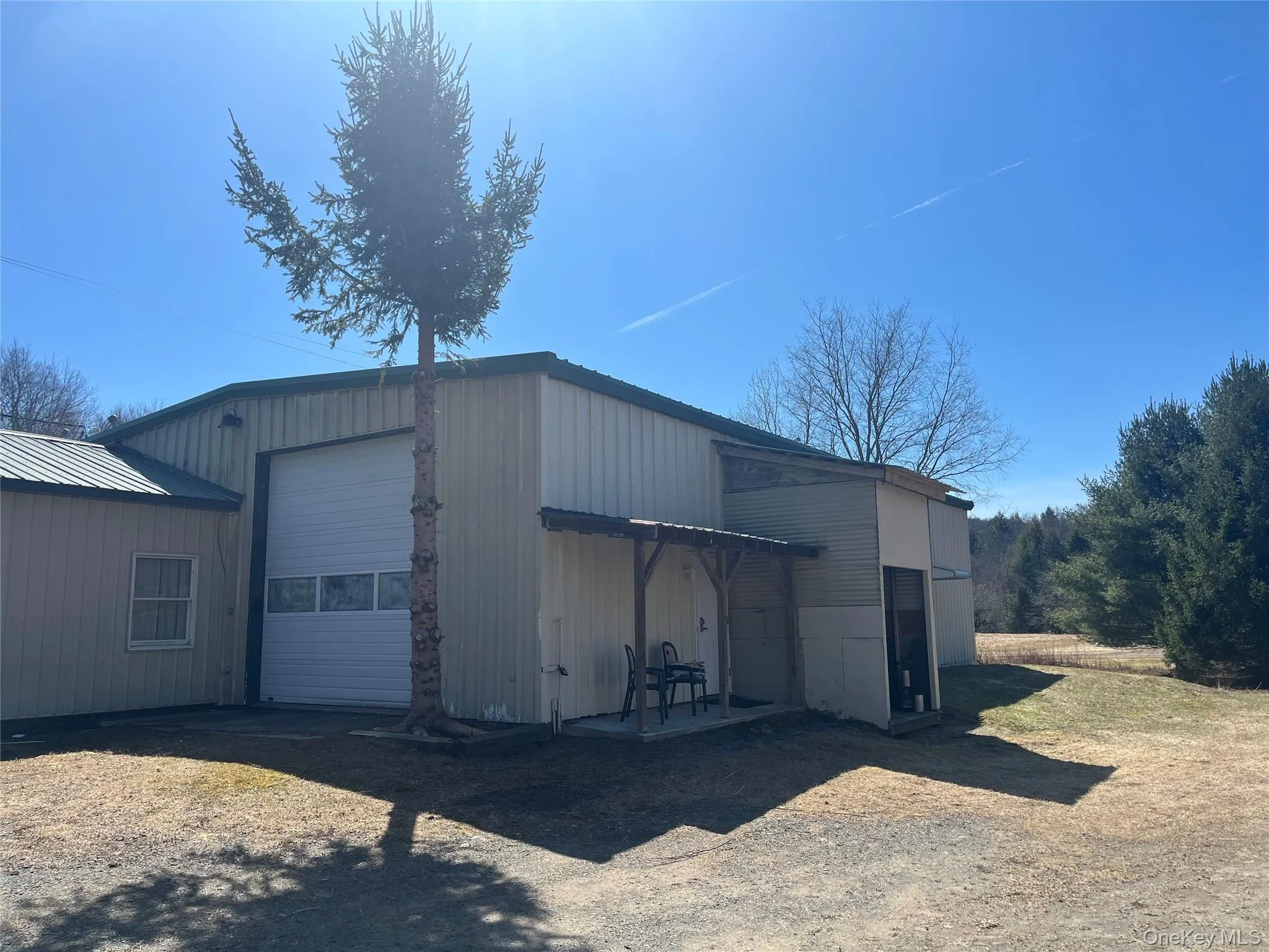 Metal-sided structure featuring a large overhead door with window panels, an additional entry door, and an attached covered porch Metal-sided structure featuring a large overhead door with window panels, an additional entry door, and an attached covered porch