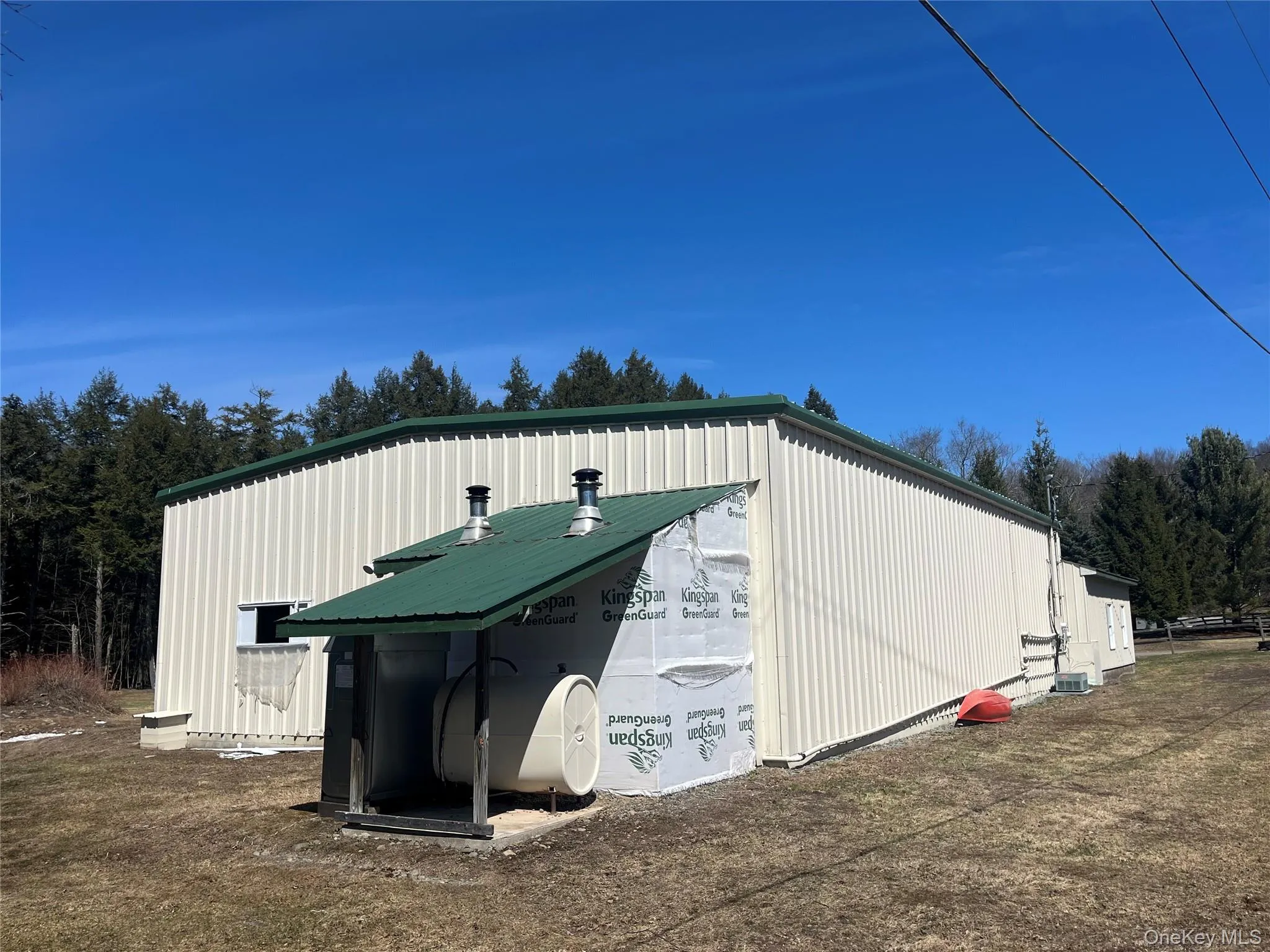 Industrial building featuring corrugated metal siding, a green metal roof, and an exposed utility structure with a matching green metal roof Industrial building featuring corrugated metal siding, a green metal roof, and an exposed utility structure with a matching green metal roof
