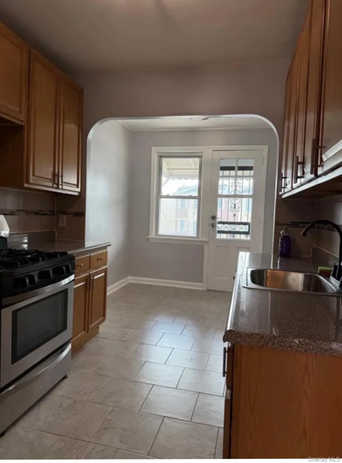 Kitchen featuring wood cabinetry, stainless steel range, a tiled backsplash, and stone-look countertops Kitchen featuring wood cabinetry, stainless steel range, a tiled backsplash, and stone-look countertops
