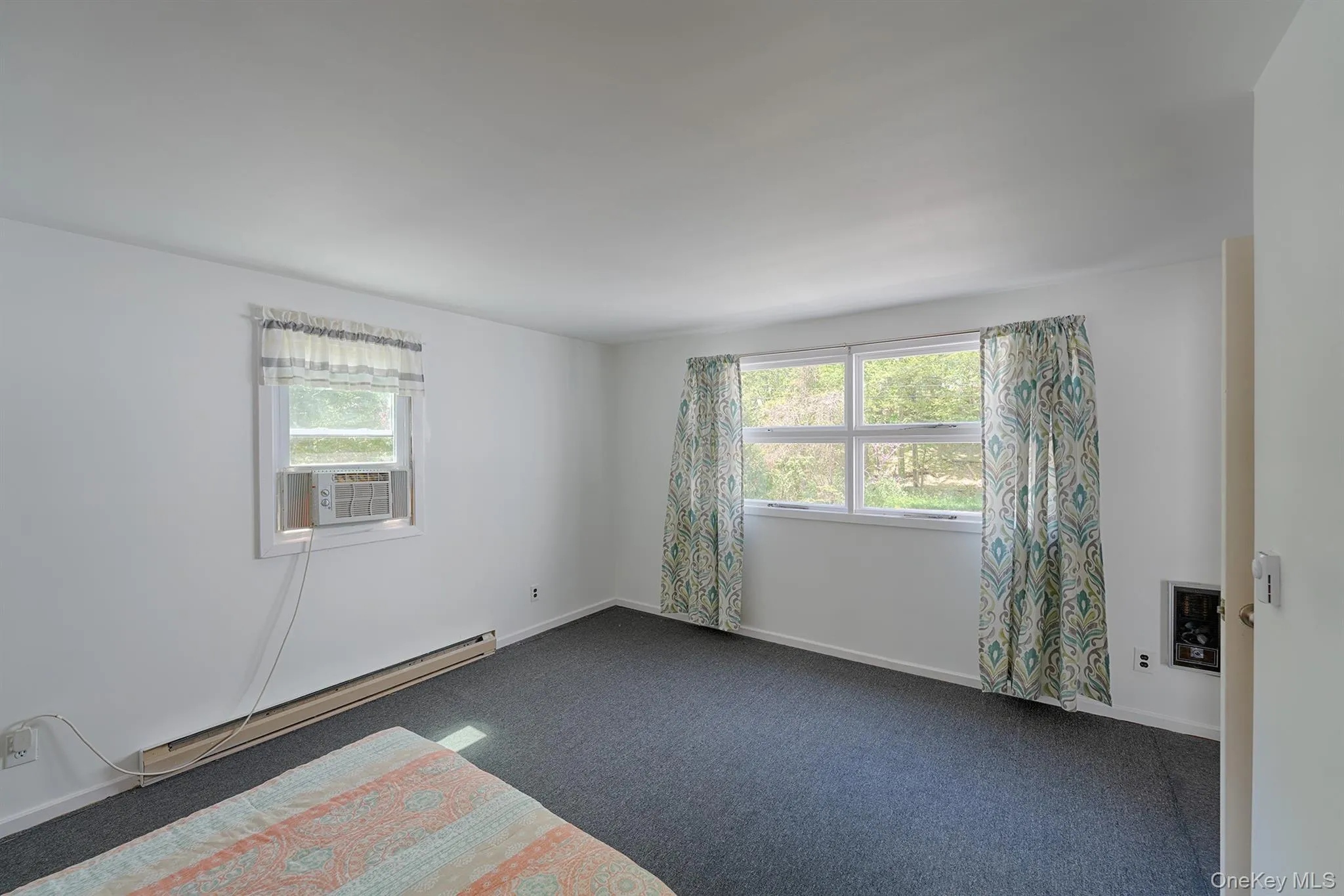 Empty room featuring plenty of natural light, cooling unit, dark colored carpet, and baseboards Empty room featuring plenty of natural light, cooling unit, dark colored carpet, and baseboards