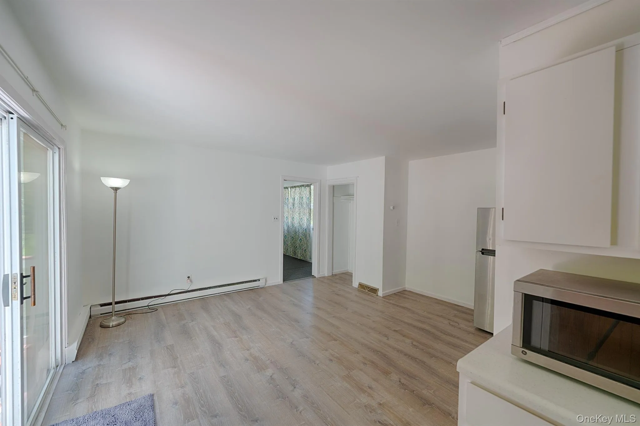 Unfurnished living room with baseboard heating, light wood-style floors, and baseboards Unfurnished living room with baseboard heating, light wood-style floors, and baseboards