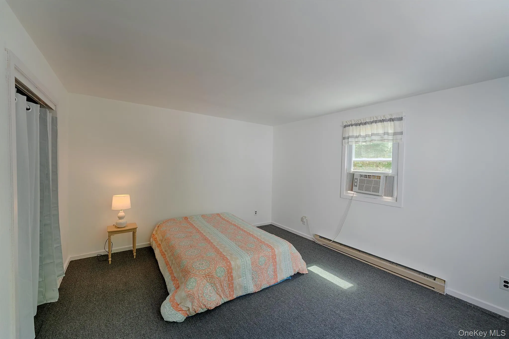 Bedroom featuring a baseboard radiator, dark colored carpet, baseboards, and cooling unit Bedroom featuring a baseboard radiator, dark colored carpet, baseboards, and cooling unit