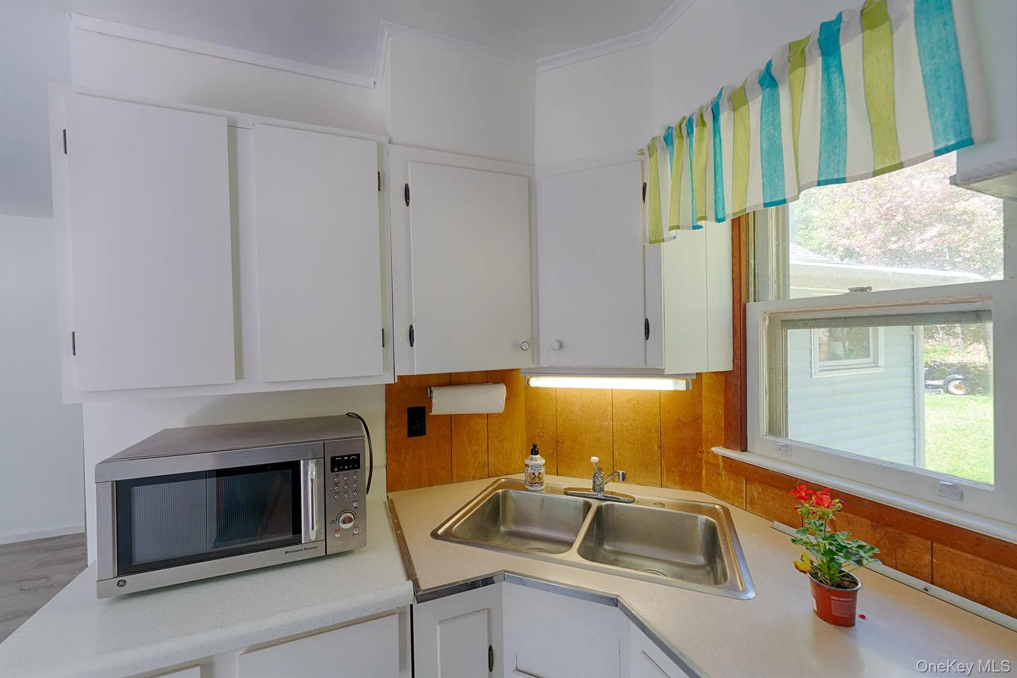 Kitchen featuring stainless steel microwave, a sink, light countertops, white cabinetry, and crown molding Kitchen featuring stainless steel microwave, a sink, light countertops, white cabinetry, and crown molding