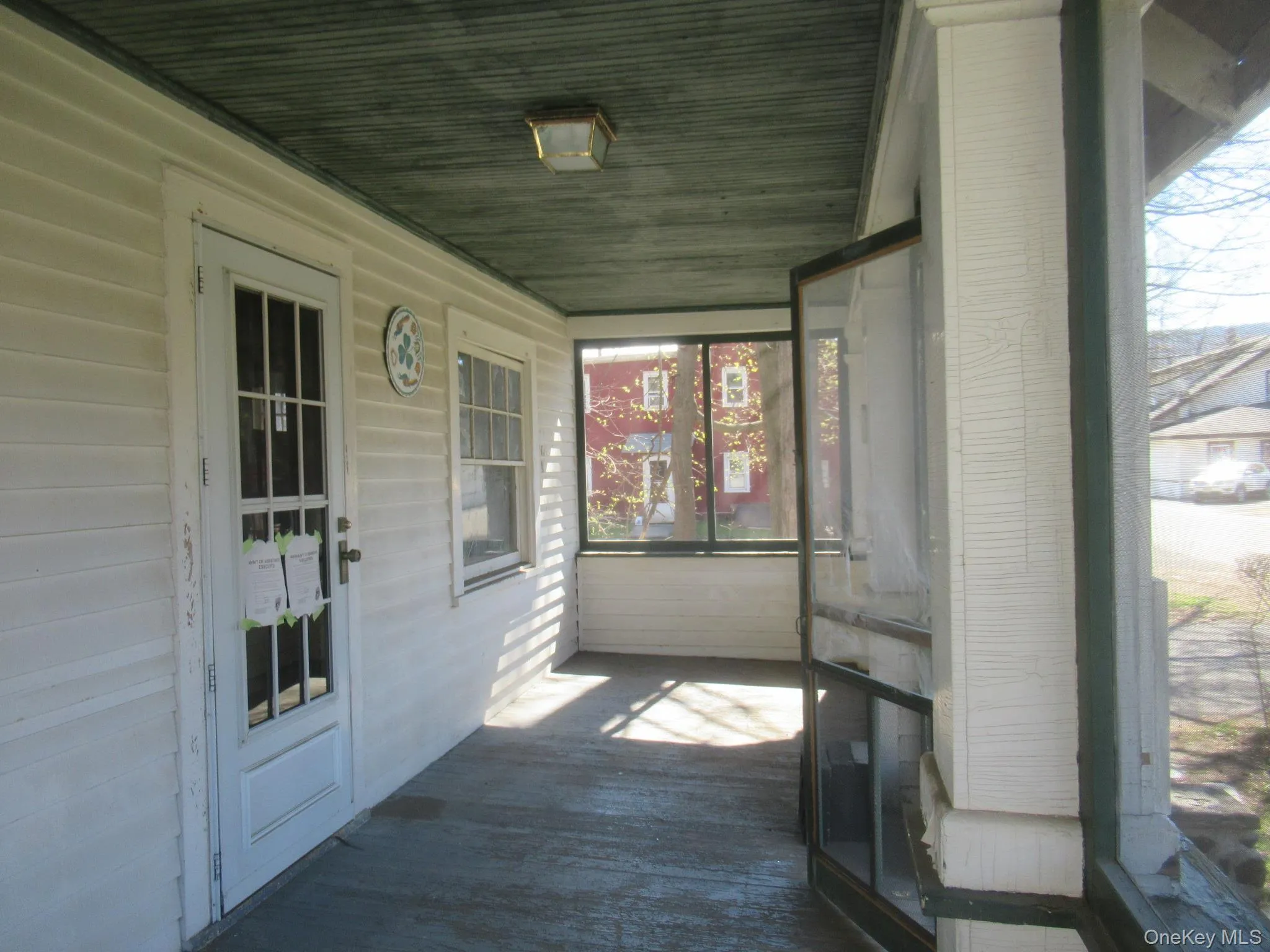 Covered porch featuring white siding, a glass-paneled entry door, a sash window, a dark green painted ceiling, and enclosed screening Covered porch featuring white siding, a glass-paneled entry door, a sash window, a dark green painted ceiling, and enclosed screening