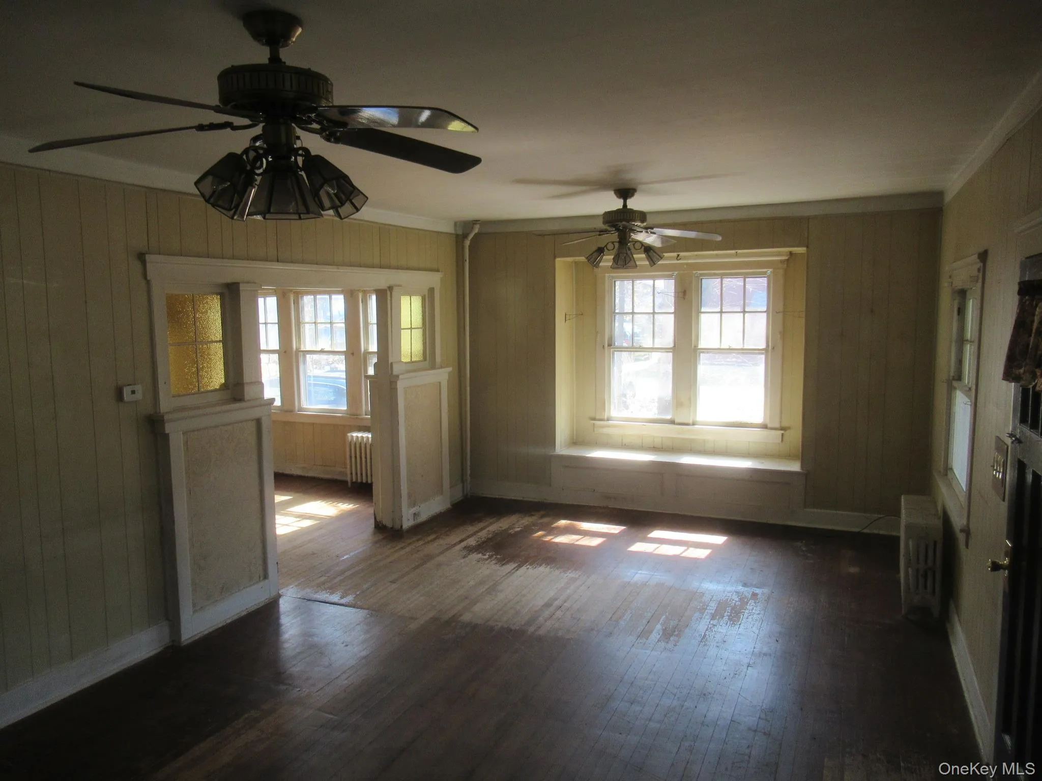 Spacious room featuring wood-finish flooring, two ceiling fans with integrated lighting, and multiple windows Spacious room featuring wood-finish flooring, two ceiling fans with integrated lighting, and multiple windows