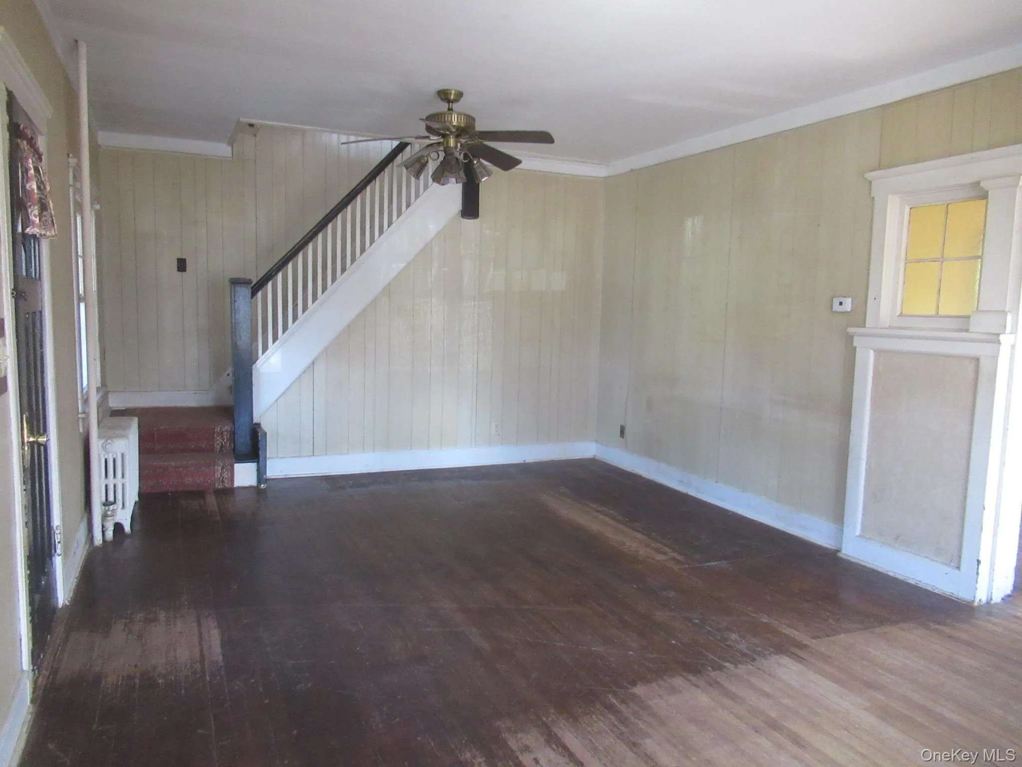 Expansive interior space featuring wood-finish flooring, a white-painted staircase with dark handrails, and a ceiling fan Expansive interior space featuring wood-finish flooring, a white-painted staircase with dark handrails, and a ceiling fan