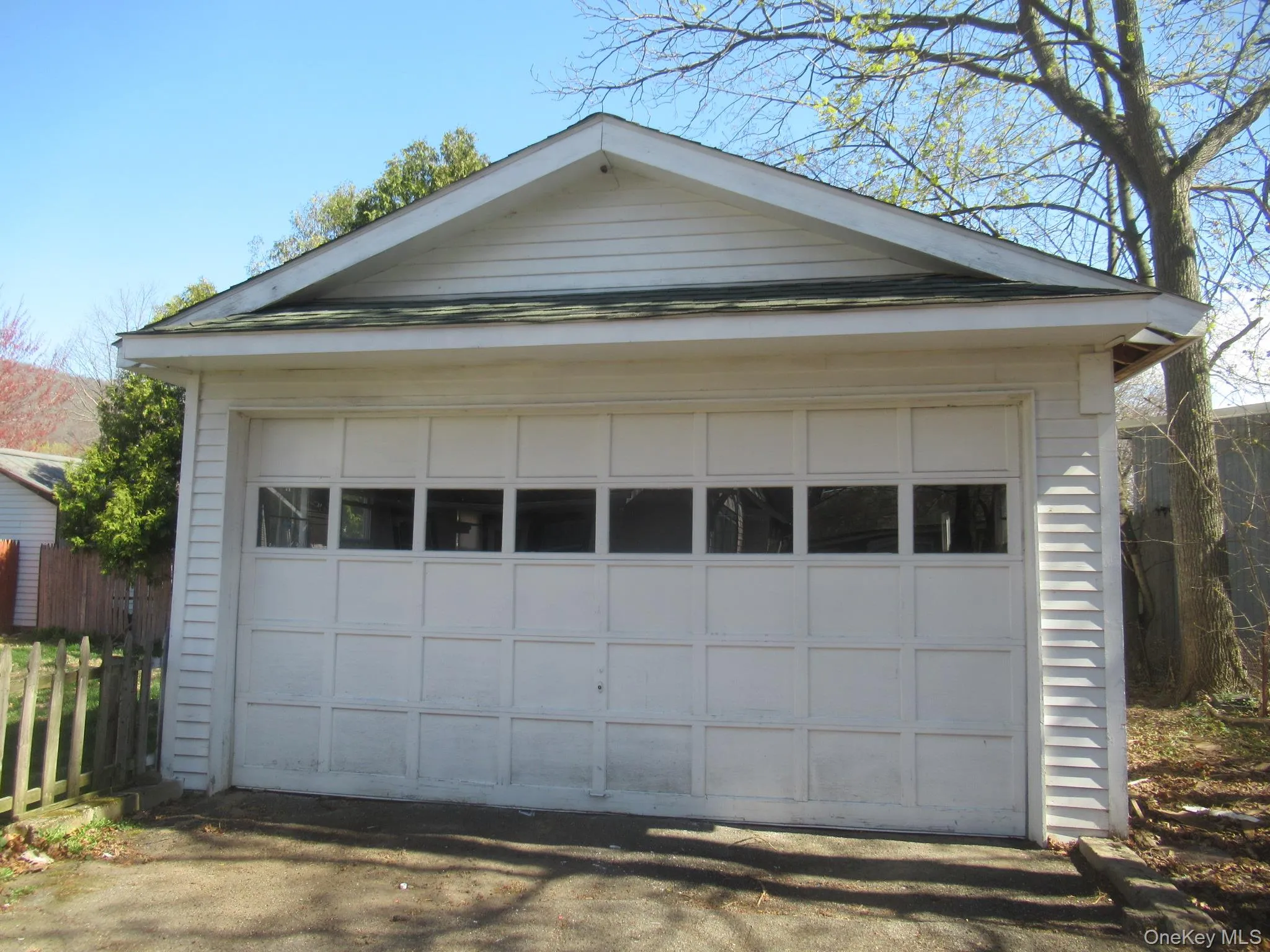 Detached garage with horizontal siding, a gabled roofline, and a panel garage door featuring upper rectangular windows Detached garage with horizontal siding, a gabled roofline, and a panel garage door featuring upper rectangular windows