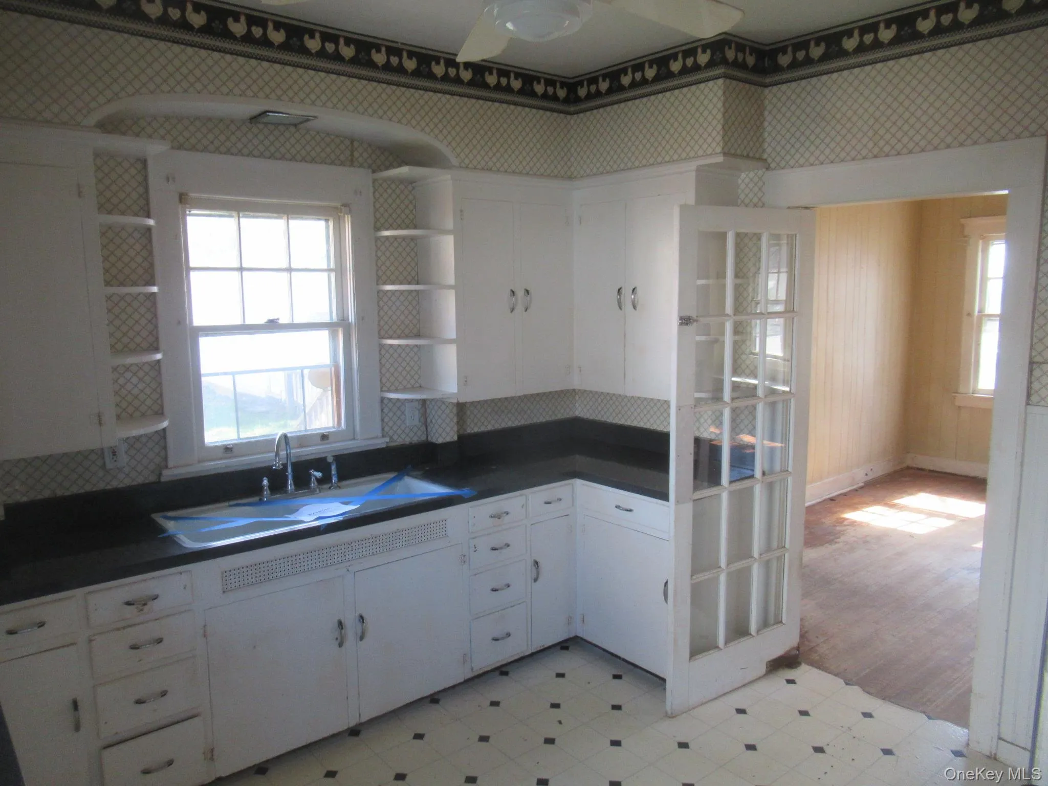 Kitchen featuring white cabinetry with integrated shelving, dark countertops, a single basin sink with a chrome faucet, and patterned floor tiling Kitchen featuring white cabinetry with integrated shelving, dark countertops, a single basin sink with a chrome faucet, and patterned floor tiling