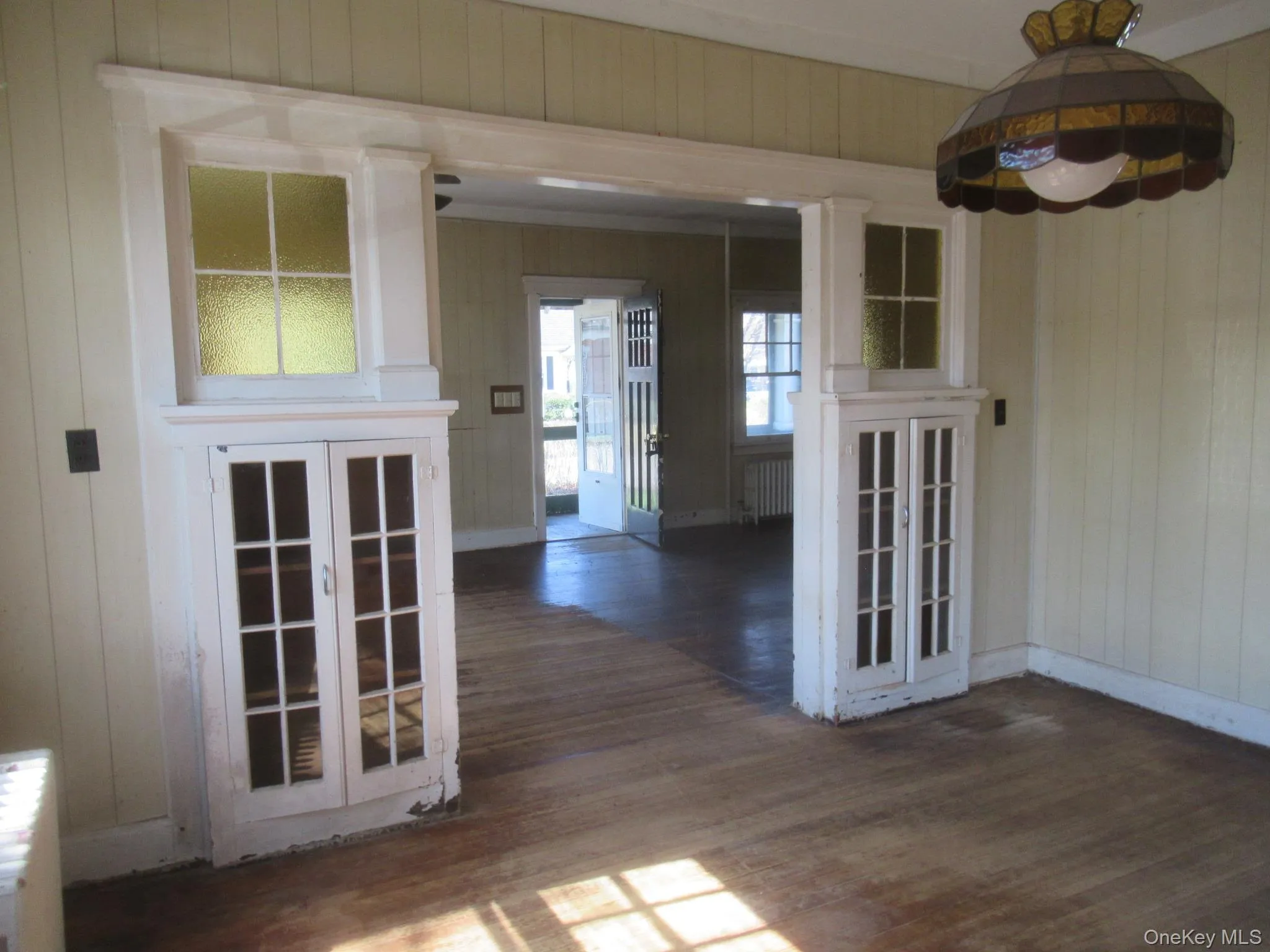 Interior room featuring wood-finish flooring, vertical paneling, and an ornate stained-glass light fixture Interior room featuring wood-finish flooring, vertical paneling, and an ornate stained-glass light fixture